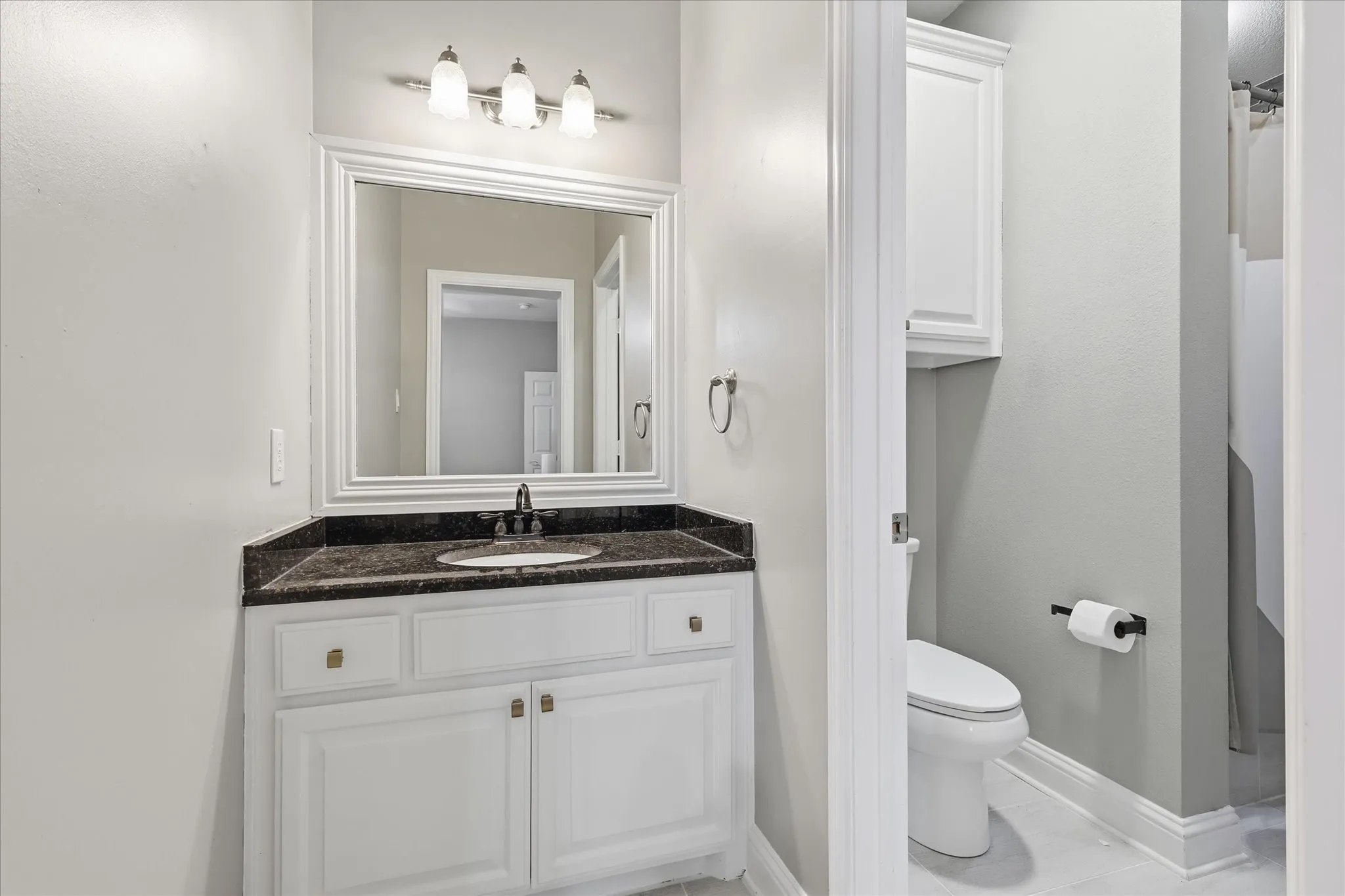 Bathroom vanity featuring a dark countertop, undermount sink, and white cabinetry with brass hardware