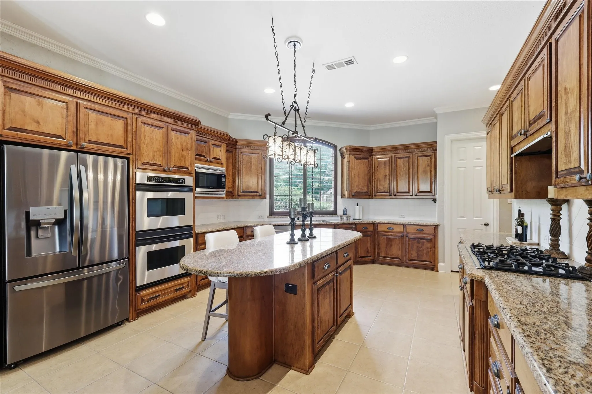 Expansive kitchen featuring a large central island with a breakfast bar, rich wood cabinetry, stainless steel appliances, and granite countertops
