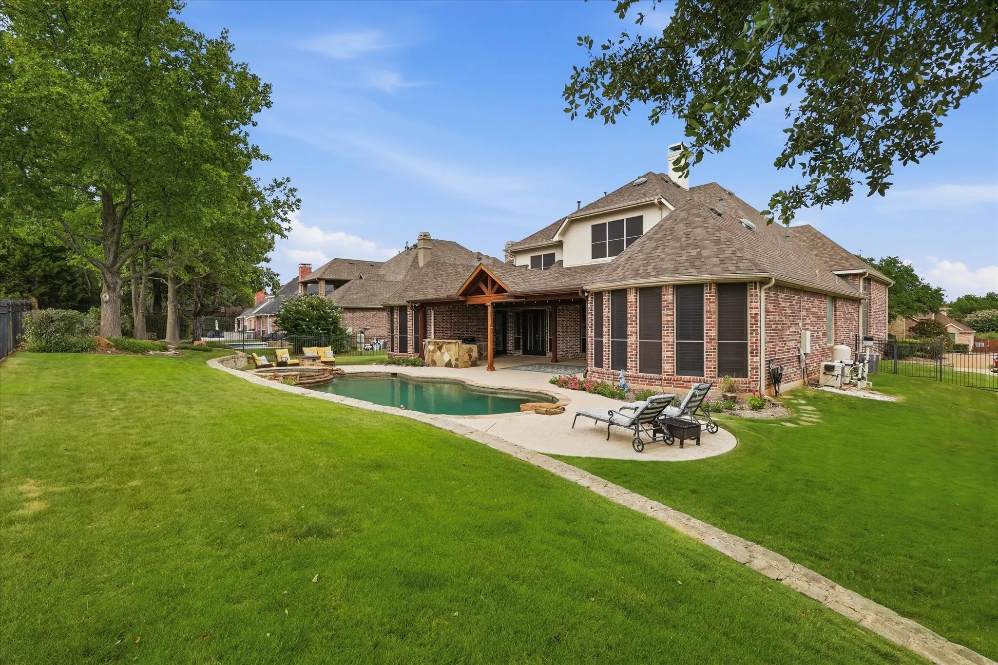 Expansive backyard featuring a curved swimming pool with stone coping, a stone patio, and a covered outdoor living area with a built-in outdoor kitchen