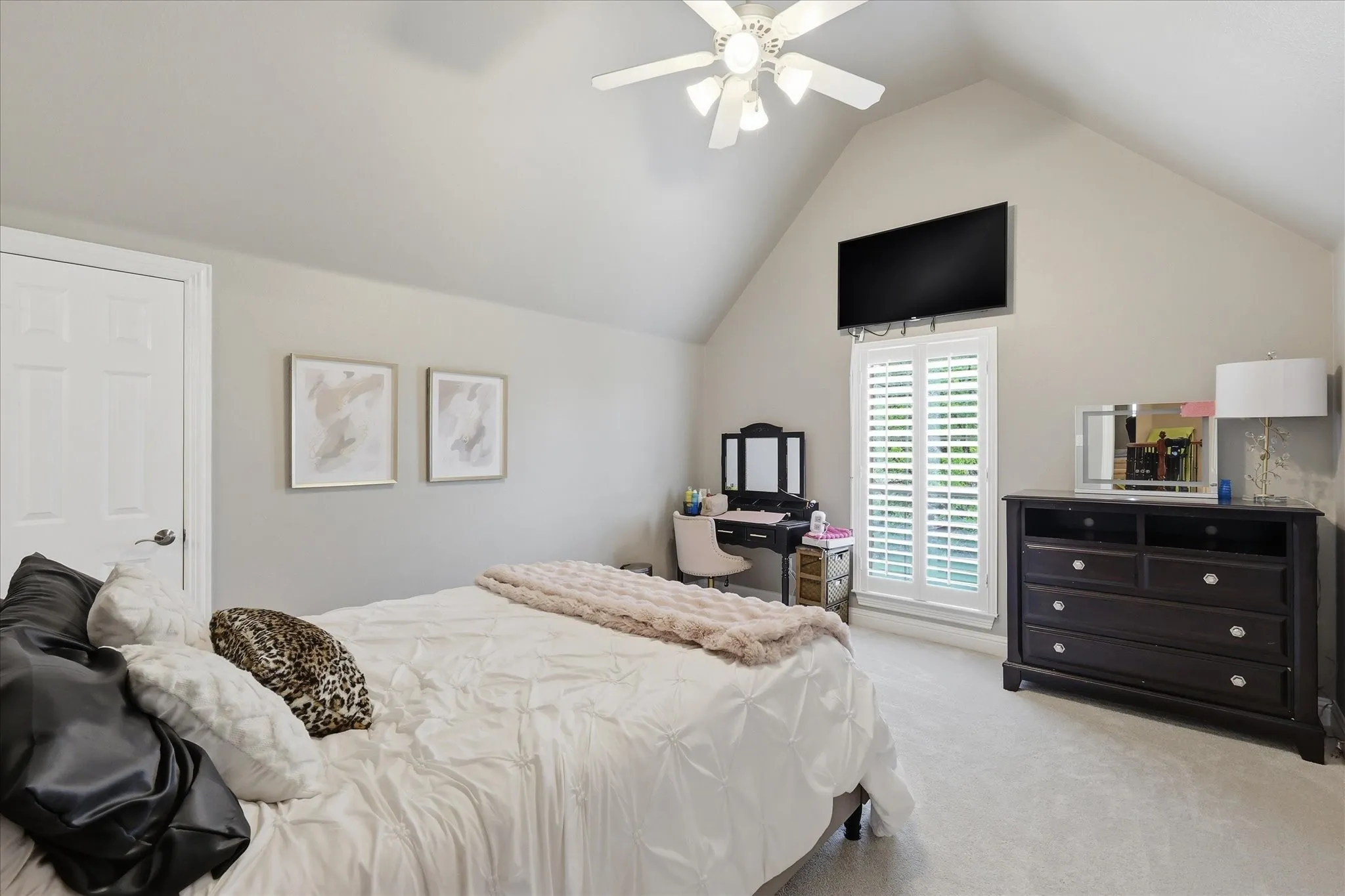 Vaulted ceiling room featuring light-toned carpeting, a window with plantation shutters, a ceiling fan with integrated lighting, and neutral wall paint