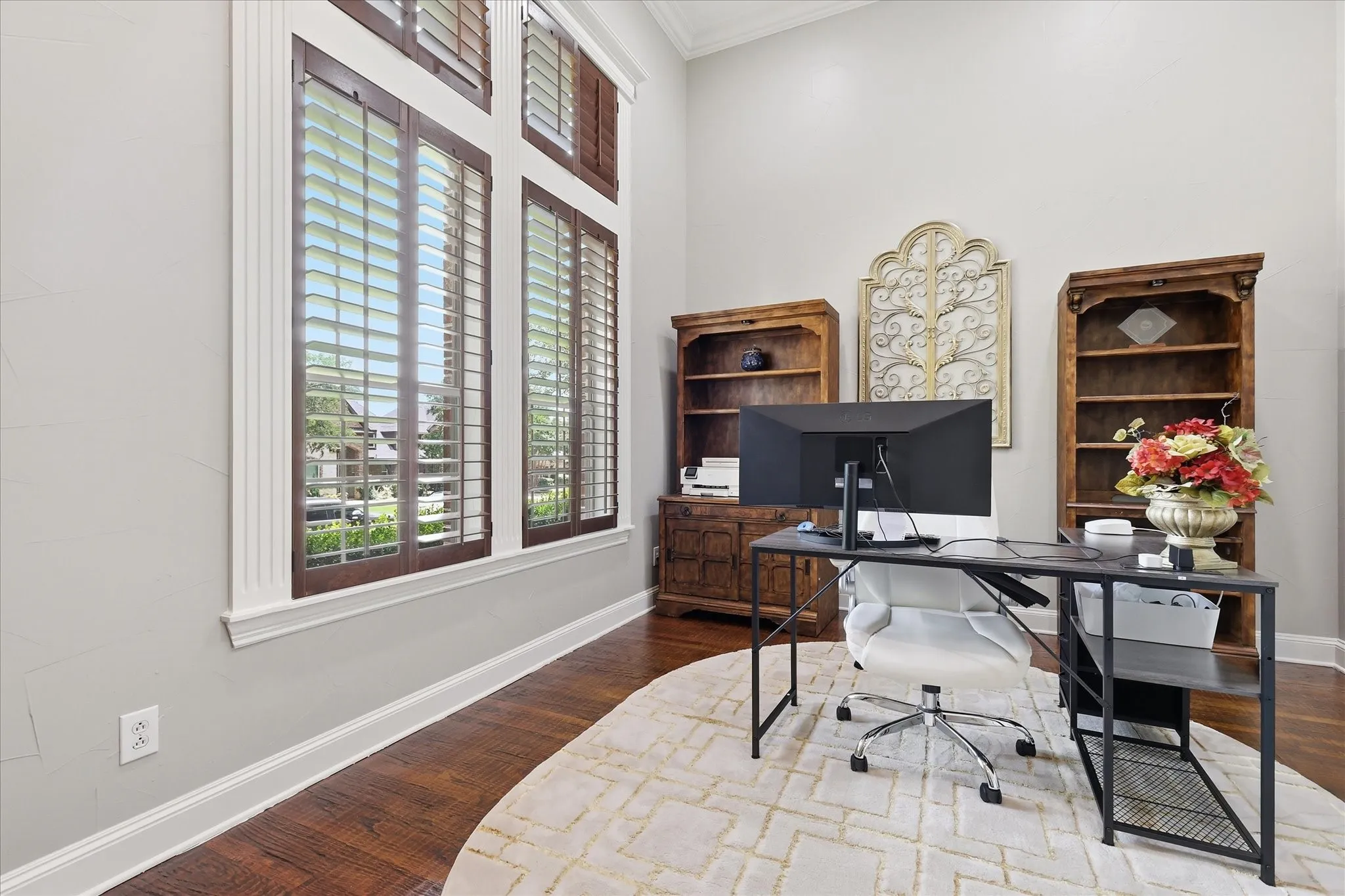 Expansive room featuring high ceilings, wood-finish flooring, tall windows with plantation shutters, and light-toned wall finishes