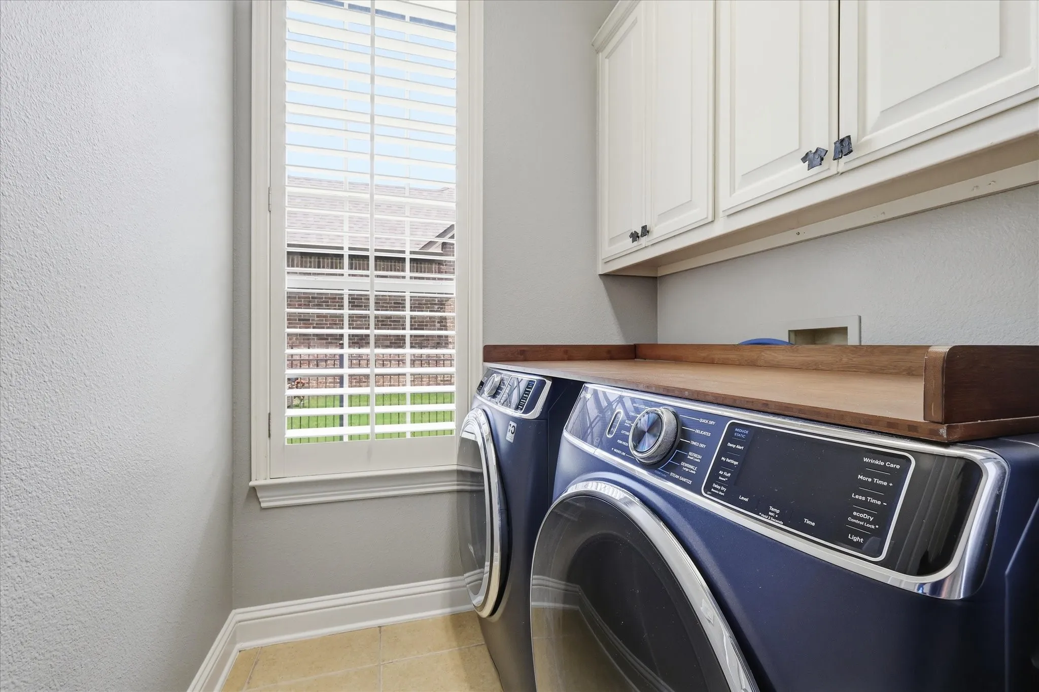 Laundry area featuring light wood-finish cabinetry, a window with plantation shutters, a wood-finish countertop, and neutral-toned wall paint