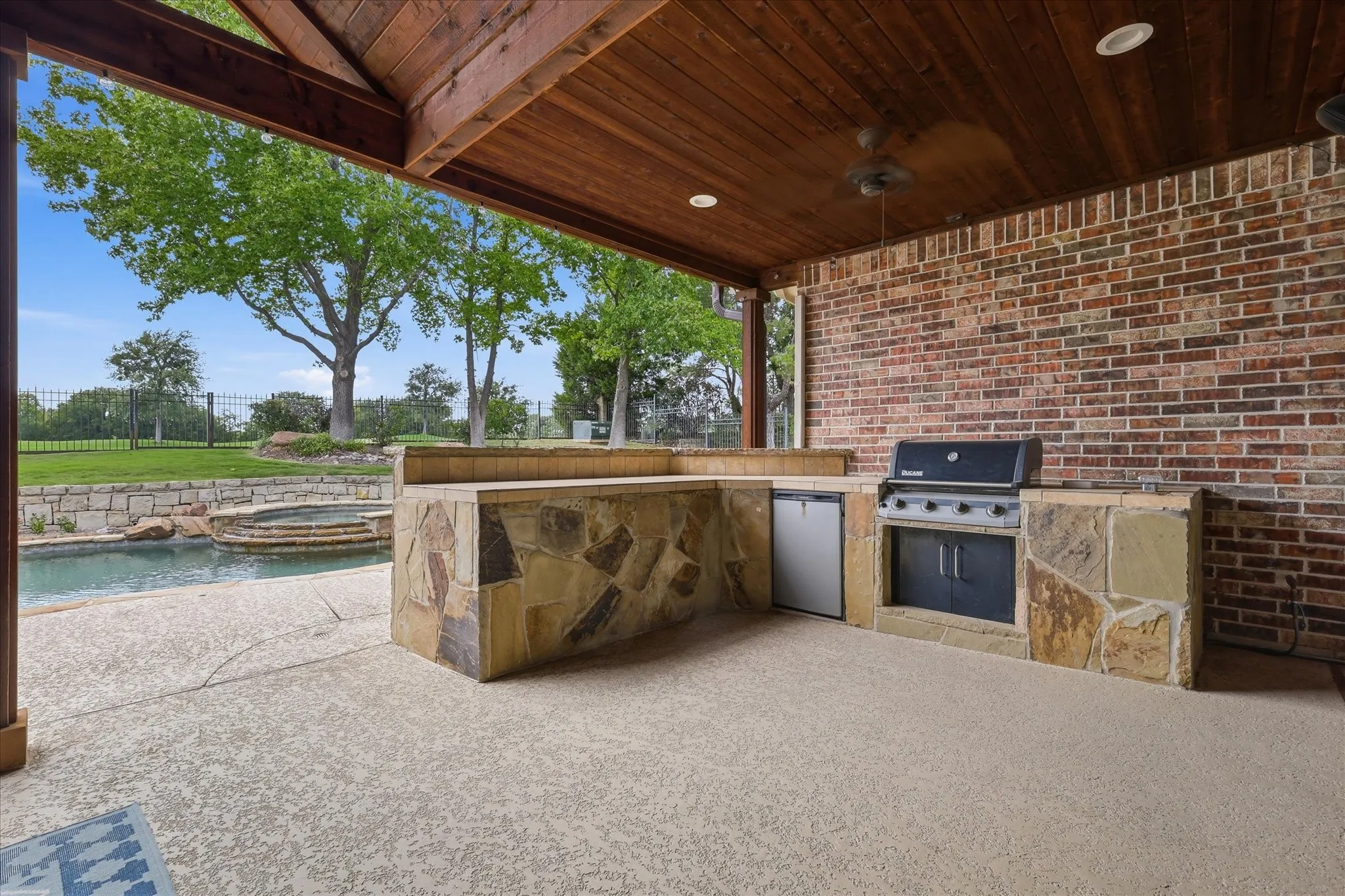 Covered outdoor living area featuring a built-in stone and brick outdoor kitchen, integrated grill, and refrigerator