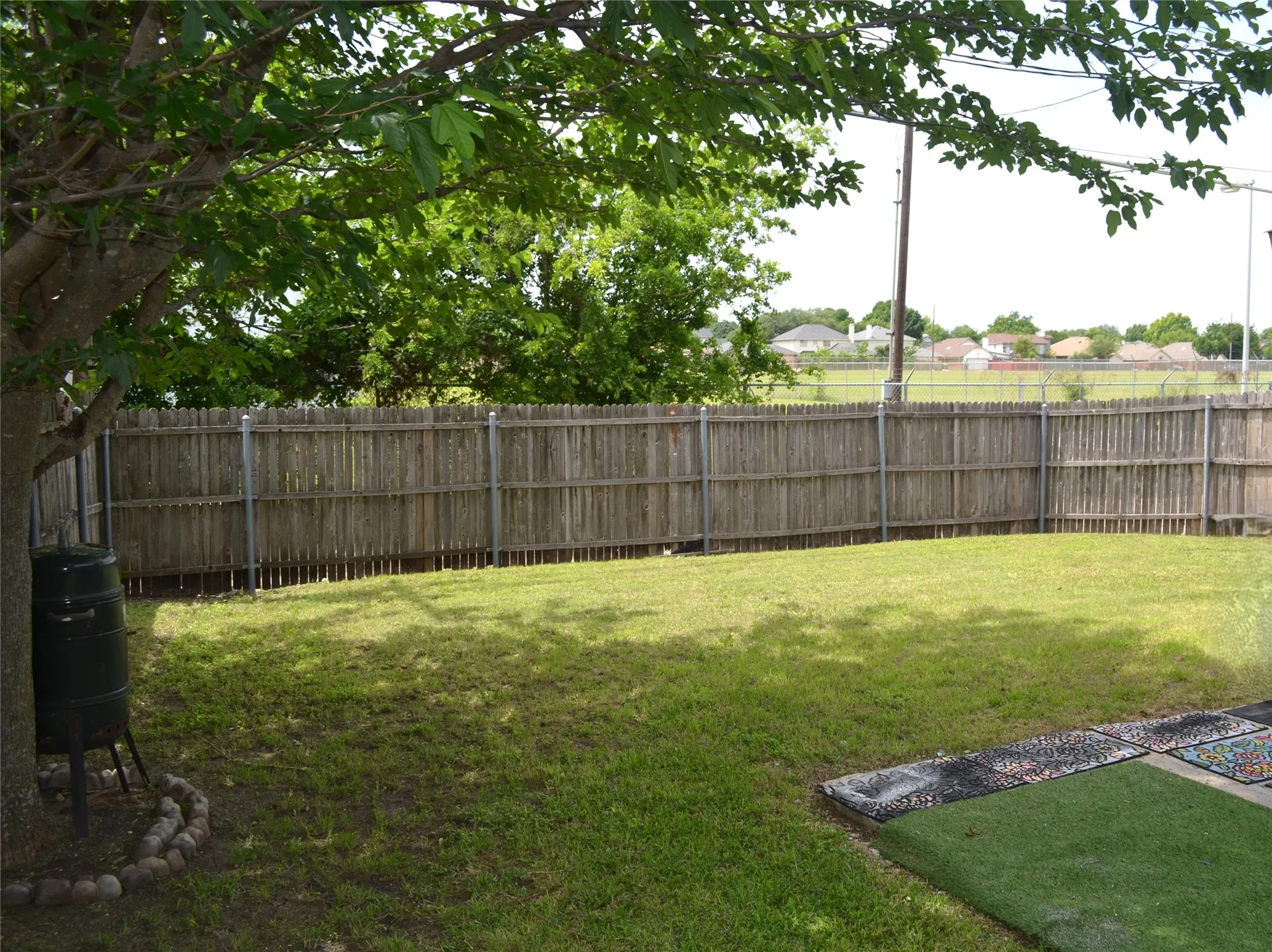 Expansive backyard featuring a wood privacy fence, mature shade tree, and a grass lawn