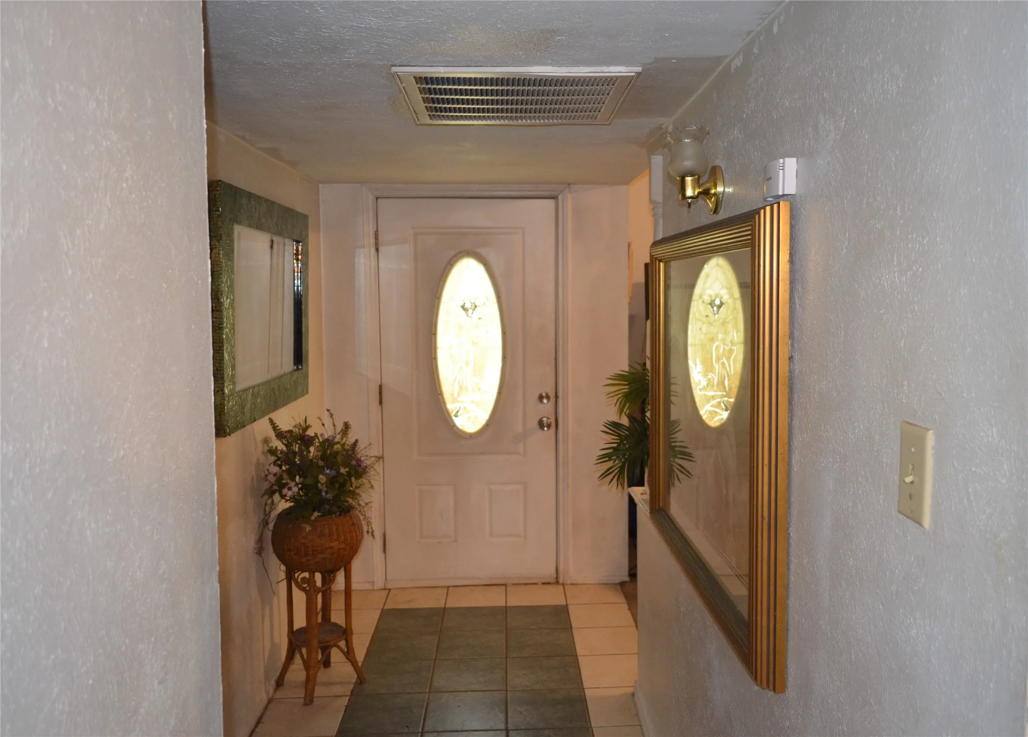 Entryway featuring a white paneled door with an oval glass insert, tile flooring, and textured wall finishes