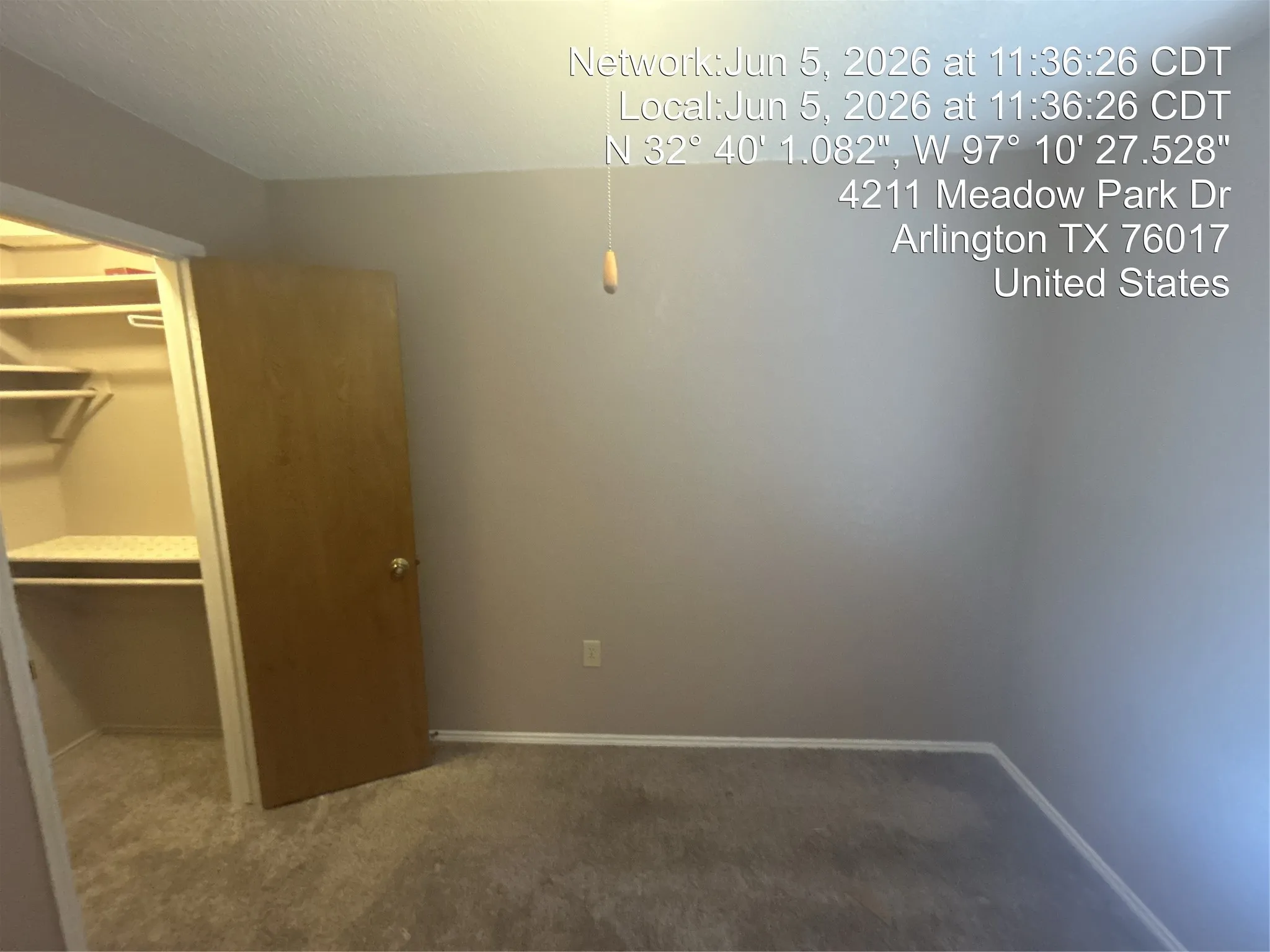 Spacious interior room featuring light gray wall paint, gray carpeting, a light wood-finish door, and a walk-in closet with built-in shelving