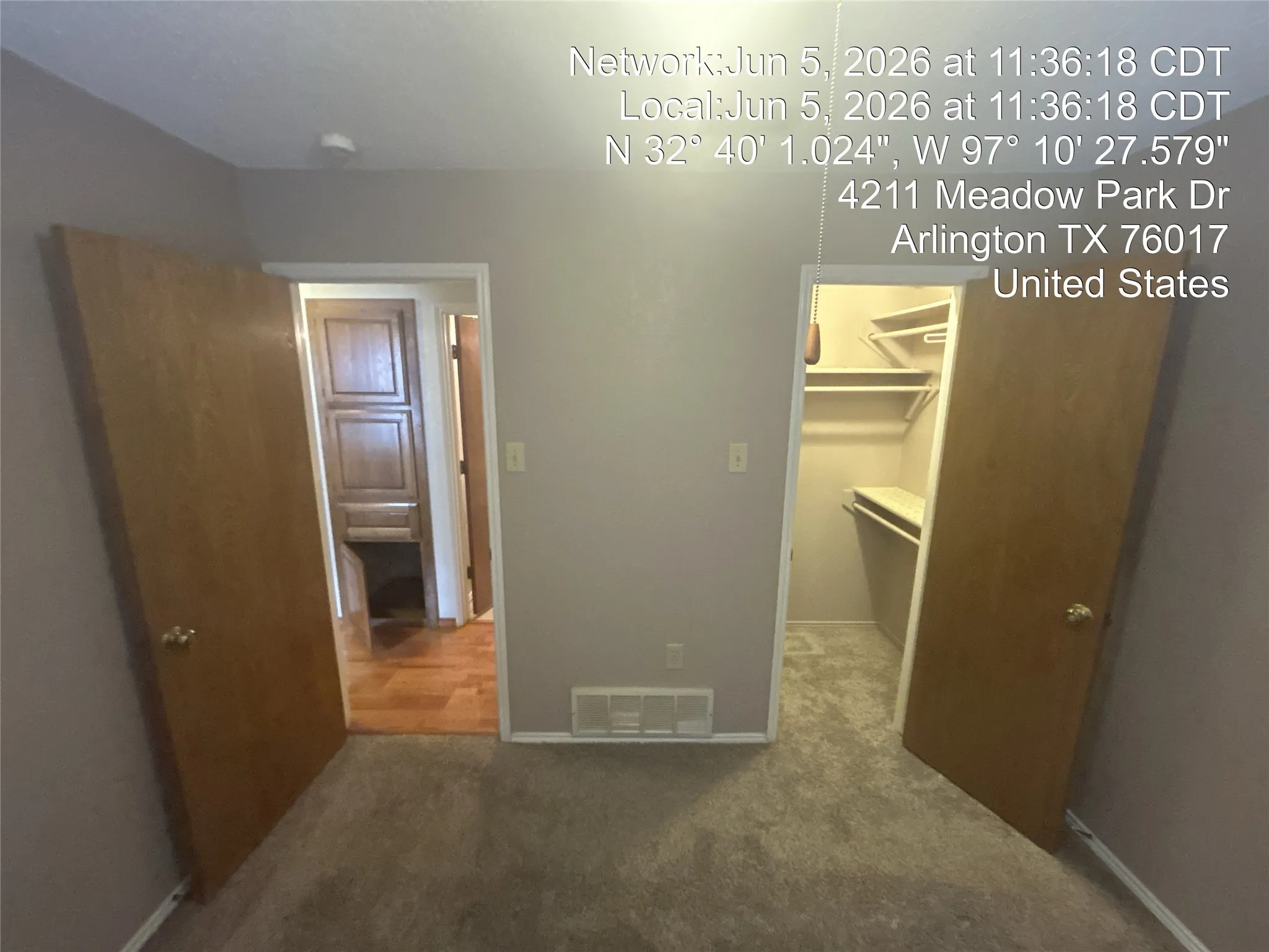Carpeted room featuring a light gray wall color, two wood-finish doors, a closet with shelving, and a doorway leading to a space with wood-finish flooring and built-in cabinetry