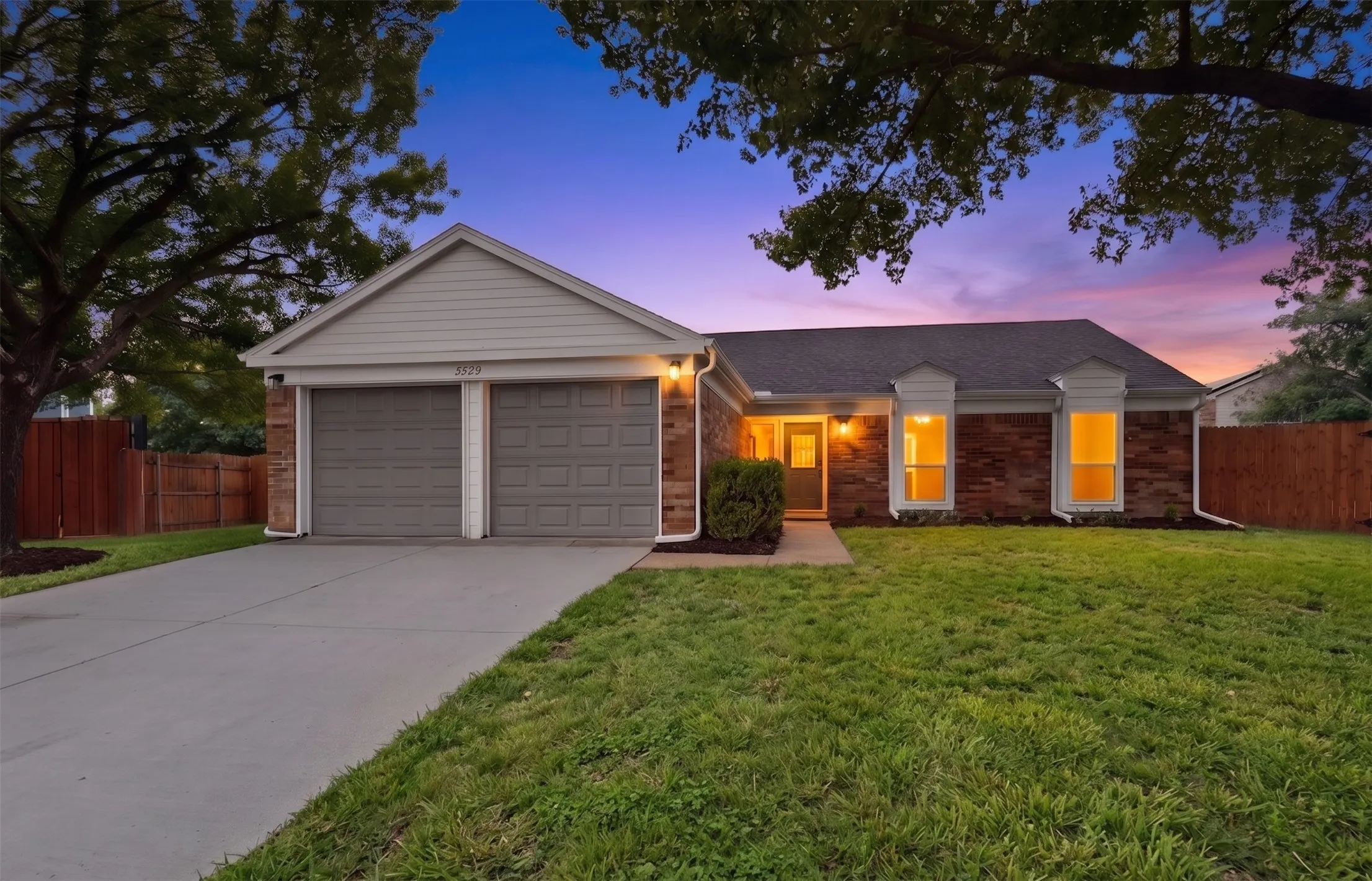 Single-story residence featuring brick and siding exterior, a two-car garage with individual doors, a concrete driveway, and a front yard with established landscaping