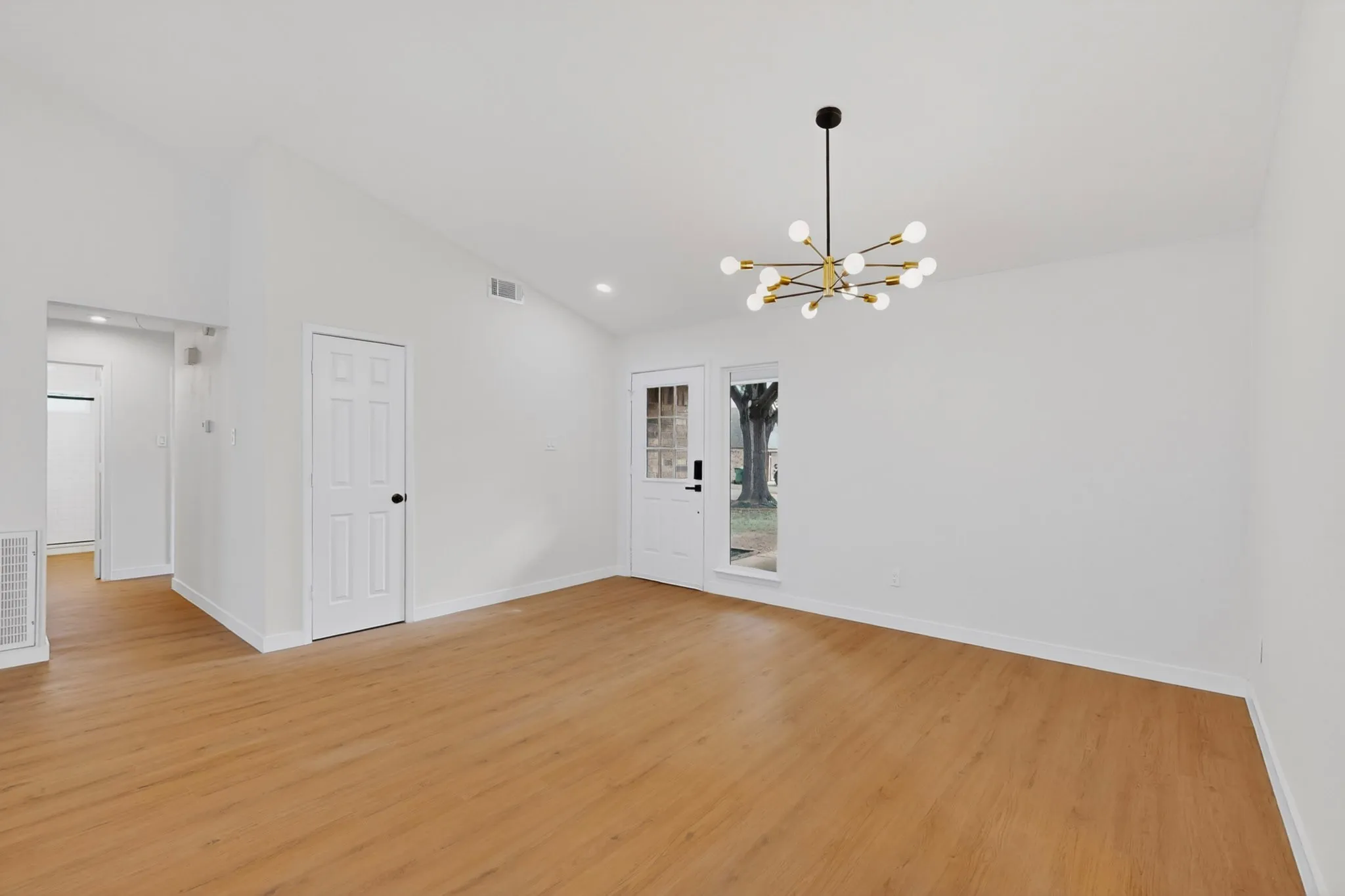 Vaulted ceilings featuring a modern sputnik chandelier, light wood-finish flooring, and crisp white walls