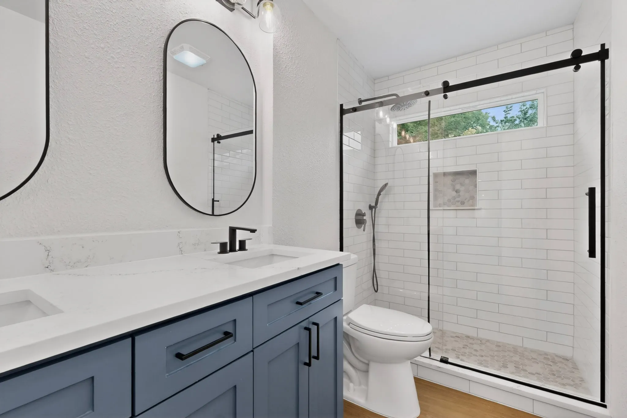 Bathroom featuring a dual vanity with a light-toned countertop, matte black hardware, and oval mirrors