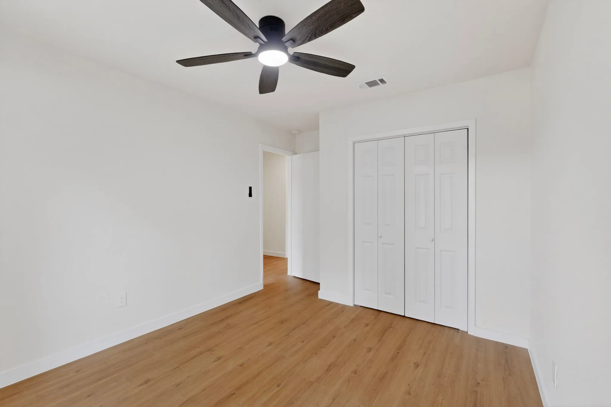 Room featuring wood-finish flooring, crisp white walls, and a contemporary ceiling fan with integrated lighting