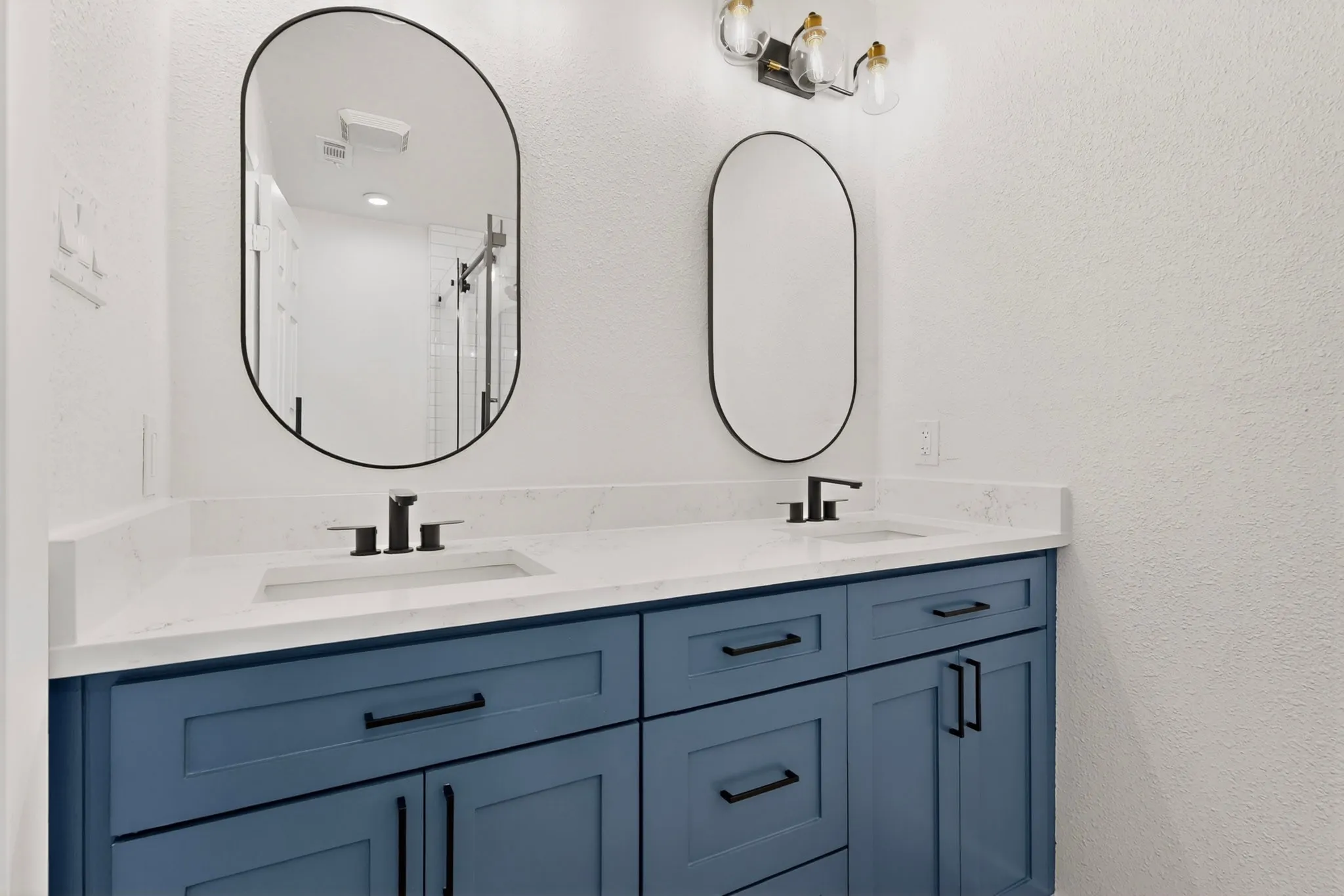 Double vanity featuring a blue wood-finish cabinet, quartz-look countertop, integrated sinks, and matte black fixtures
