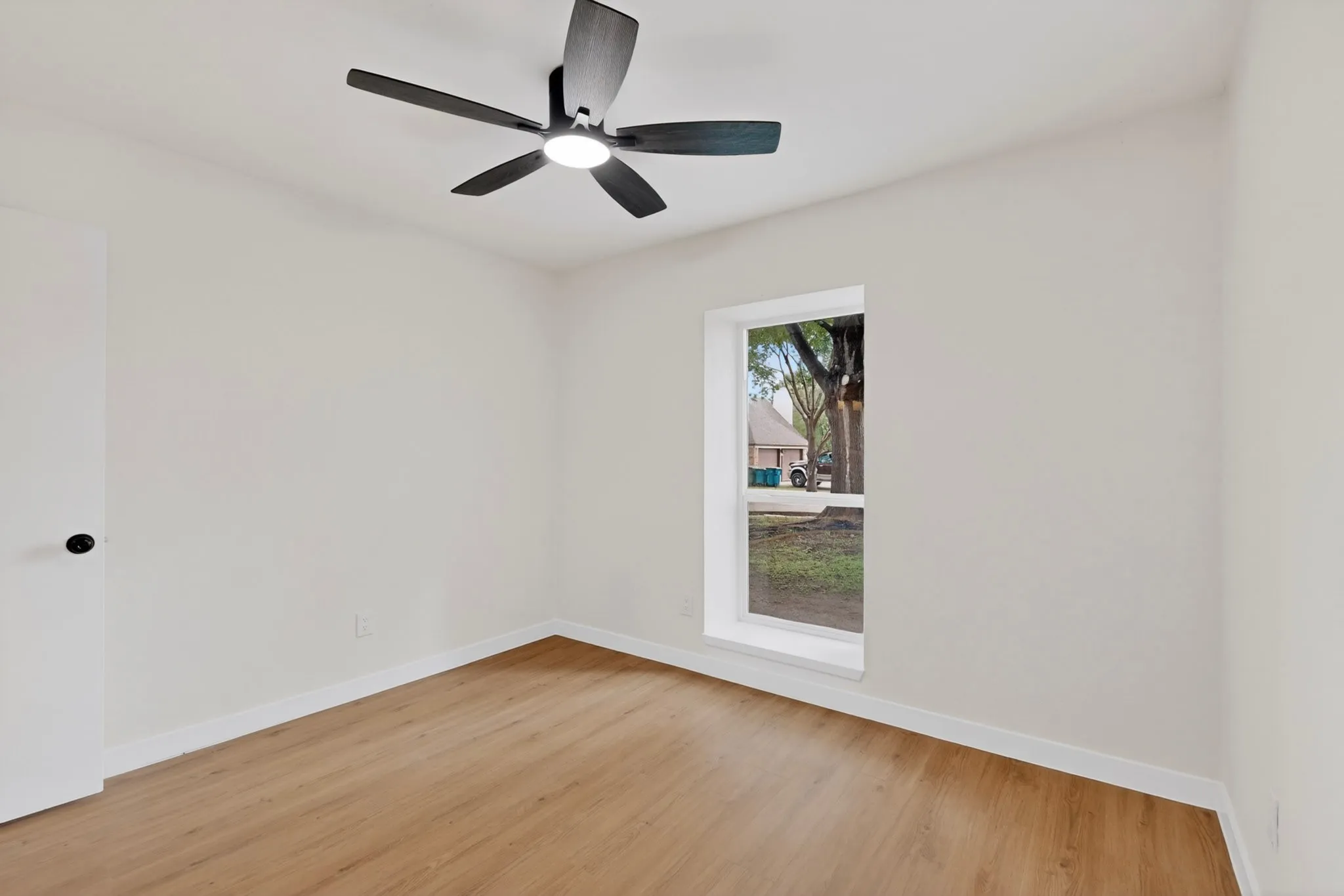 Bright interior space featuring wood-finish flooring, a contemporary ceiling fan with integrated lighting, and a window with white trim