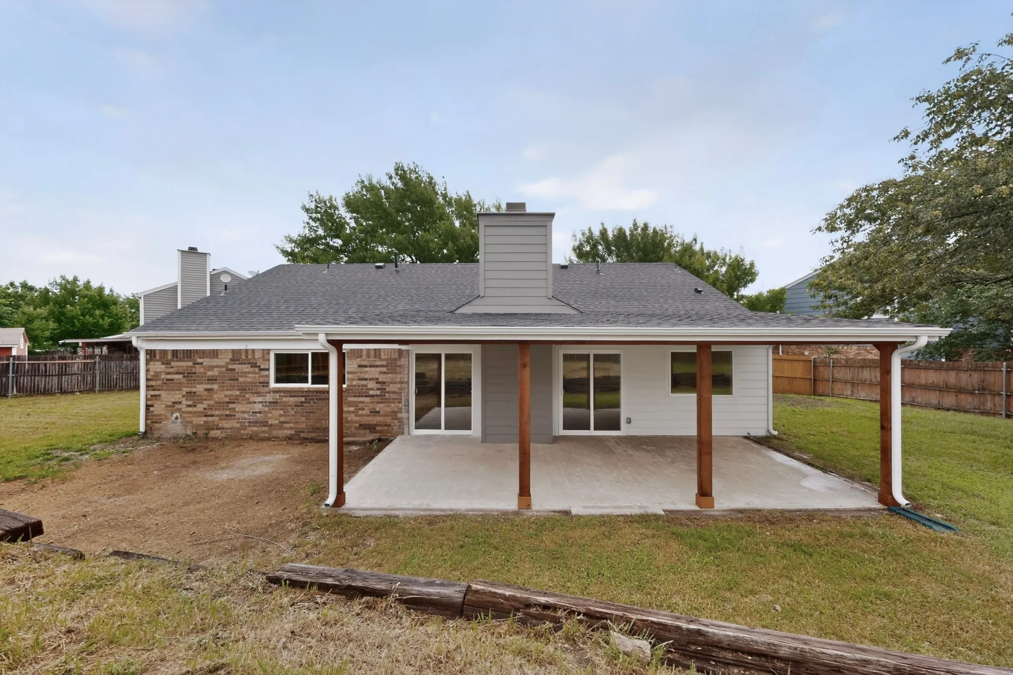 Rear exterior featuring a covered patio with a concrete slab, wooden support beams, and a white gutter system
