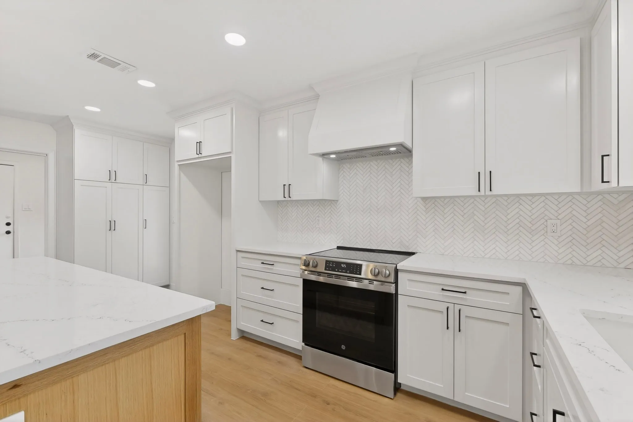 Modern kitchen featuring white cabinetry with matte black hardware, white countertops, and a herringbone pattern tile backsplash