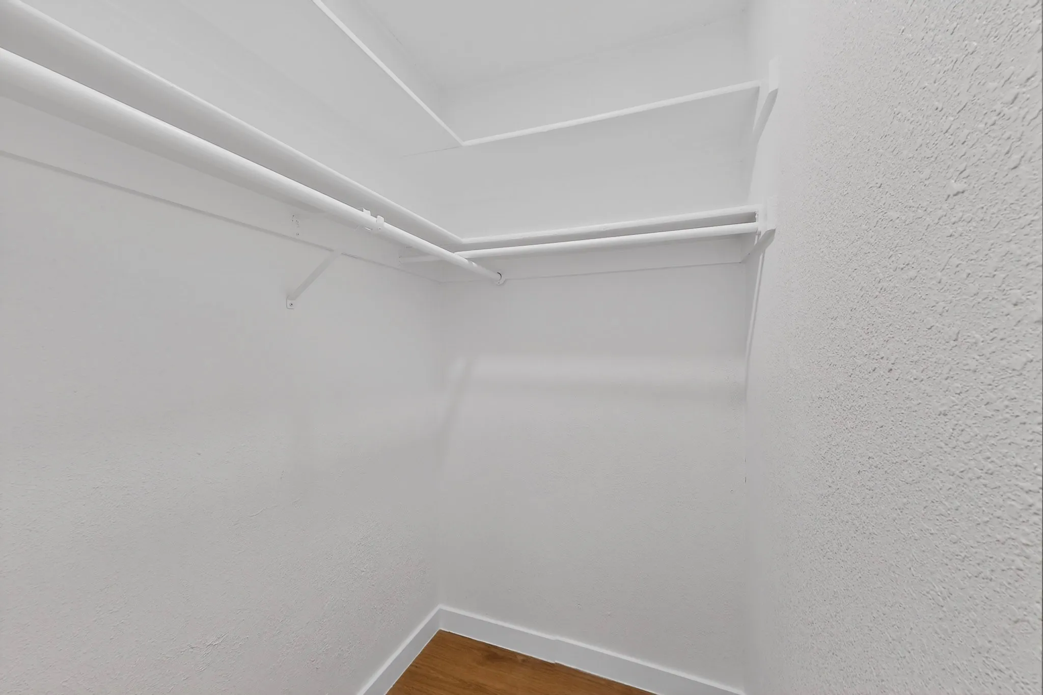 Spacious closet featuring multiple hanging rods, integrated shelving, white walls, and wood-finish flooring