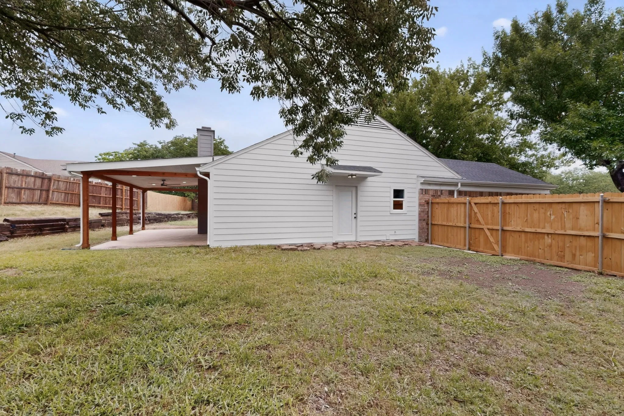 Expansive backyard featuring a covered patio structure with recessed lighting, a gravel-lined section, and a wood privacy fence
