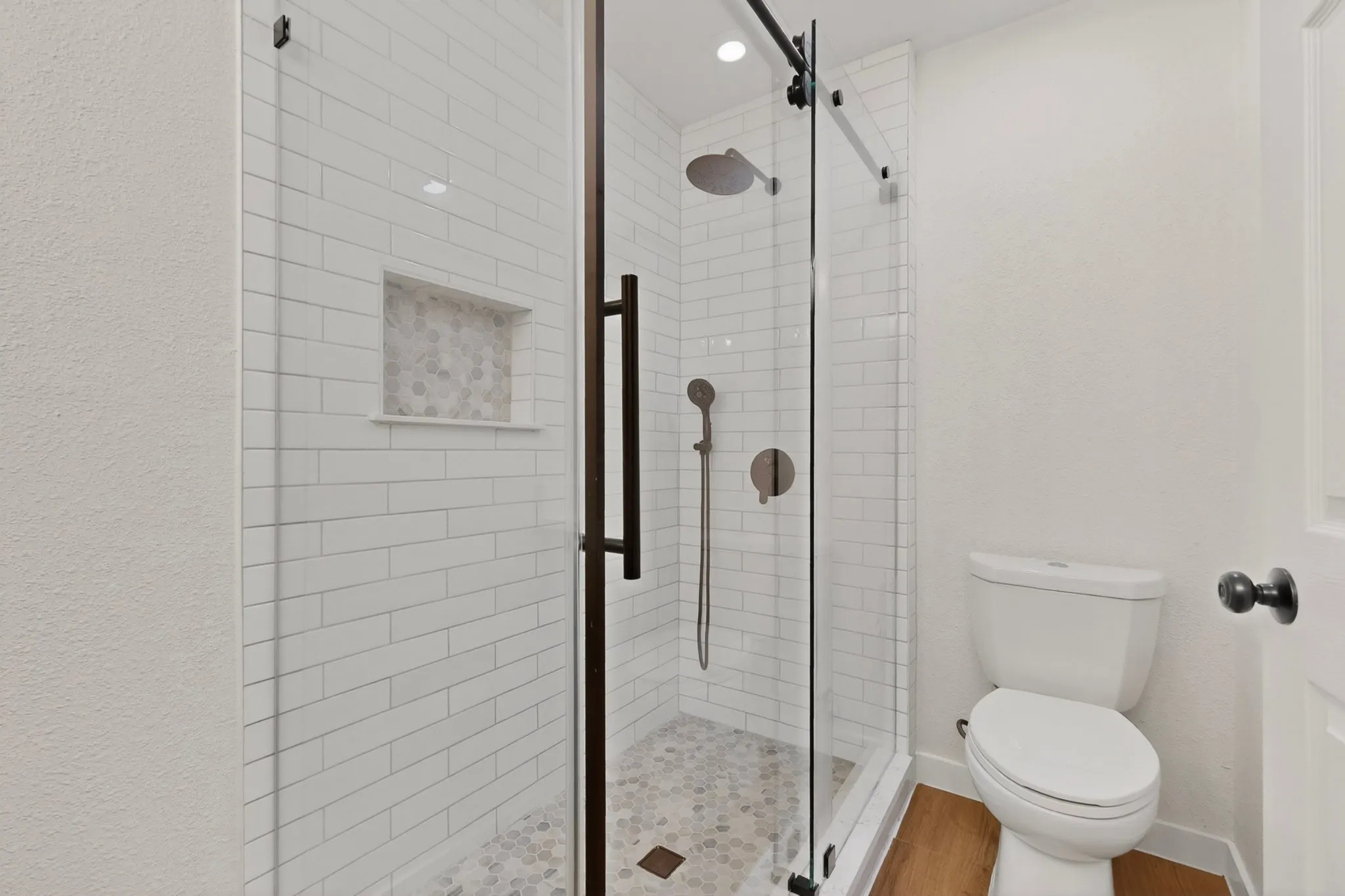 Glass-enclosed shower with subway tile surround, pebble tile flooring, and integrated niche