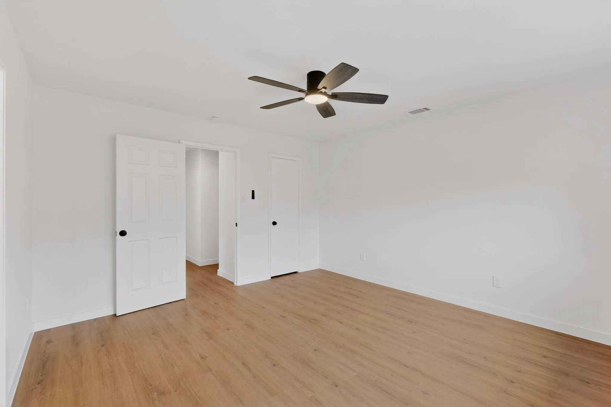 Spacious room featuring wood-finish flooring, white walls, and a modern ceiling fan with integrated lighting
