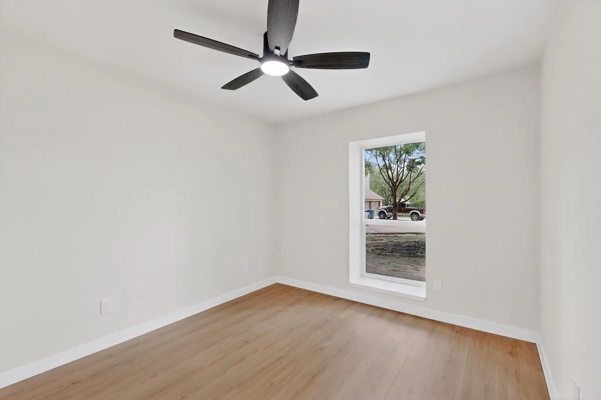 Room featuring wood-finish flooring, a contemporary ceiling fan with integrated lighting, white baseboards, and a single window with white trim