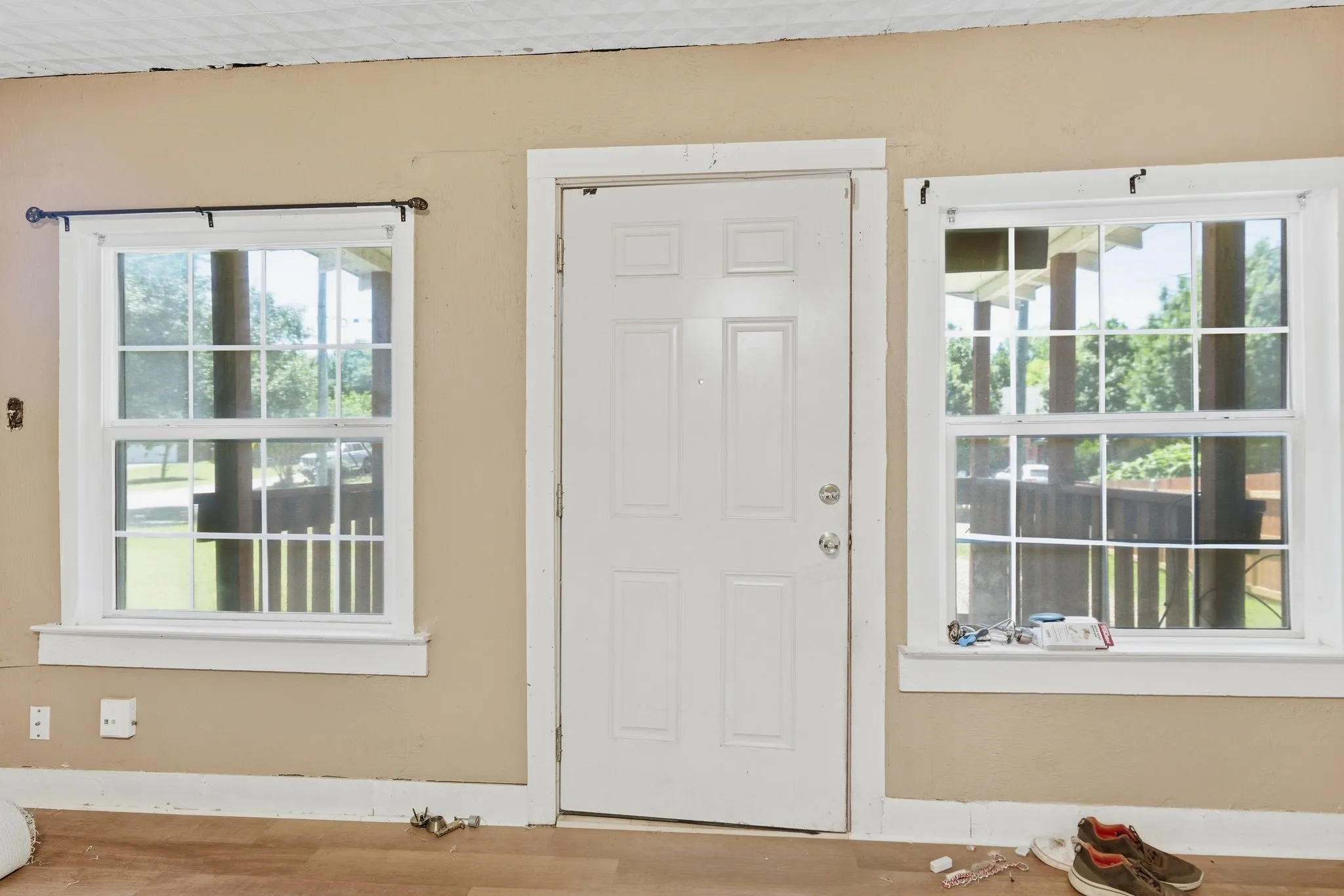 Entry door flanked by two single-hung windows with grilles, featuring light tan wall paint and wood-finish flooring