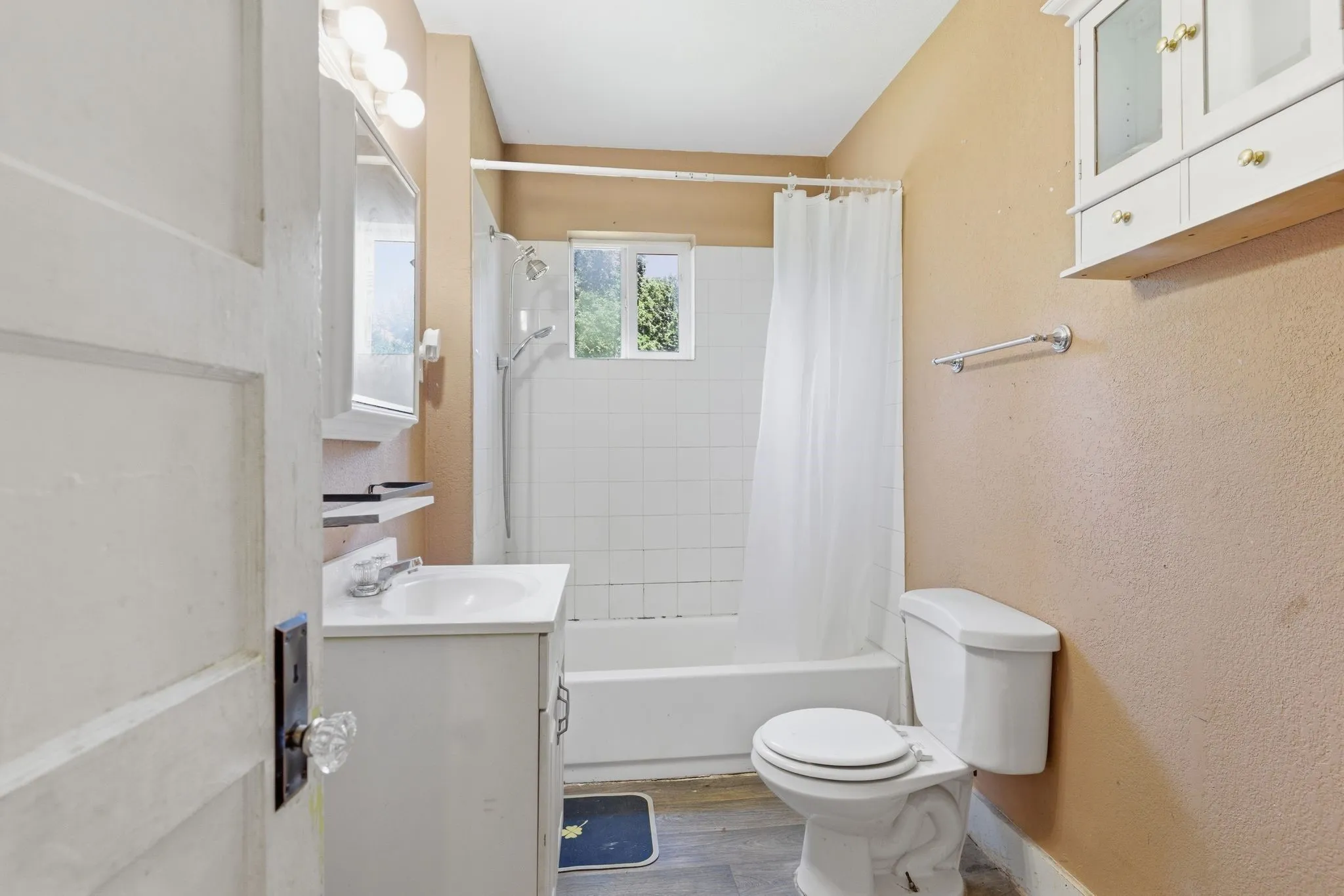 Bathroom featuring a white vanity with a single basin sink, a toilet, a tub-shower combination with white tile surround, and a wall-mounted storage cabinet