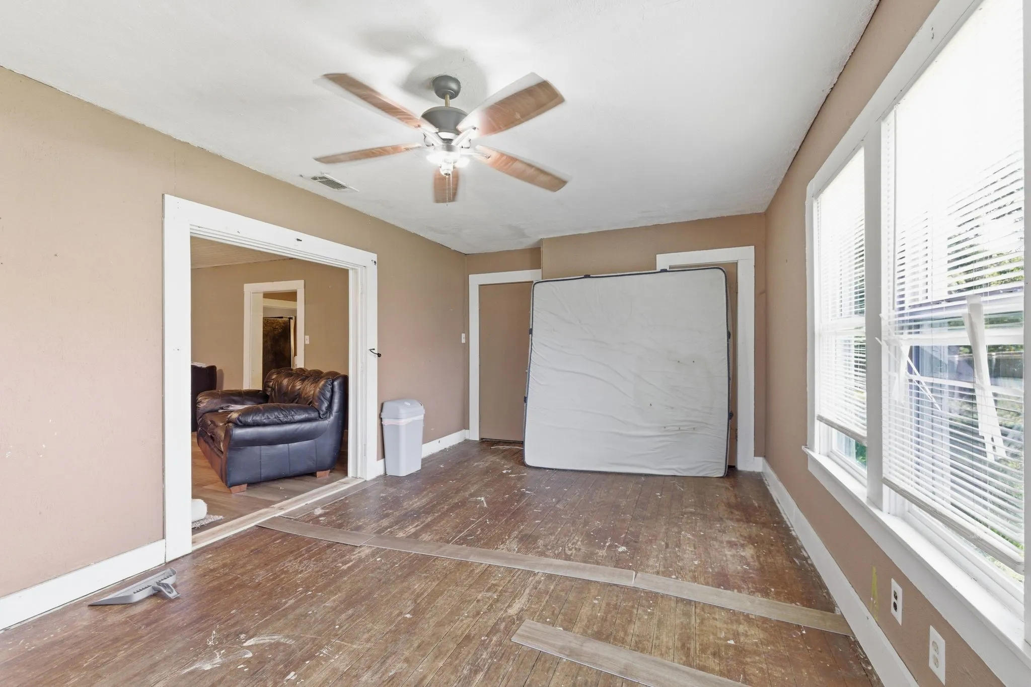 Spacious room featuring wood-finish flooring, two large windows with blinds, a ceiling fan, and painted walls with white trim