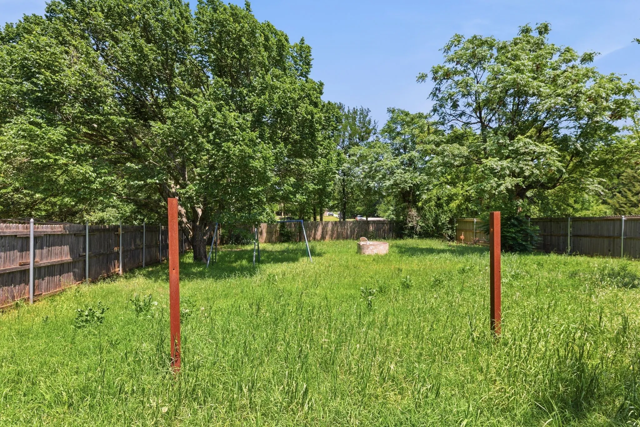 Expansive grassy yard area featuring mature trees and wood fencing