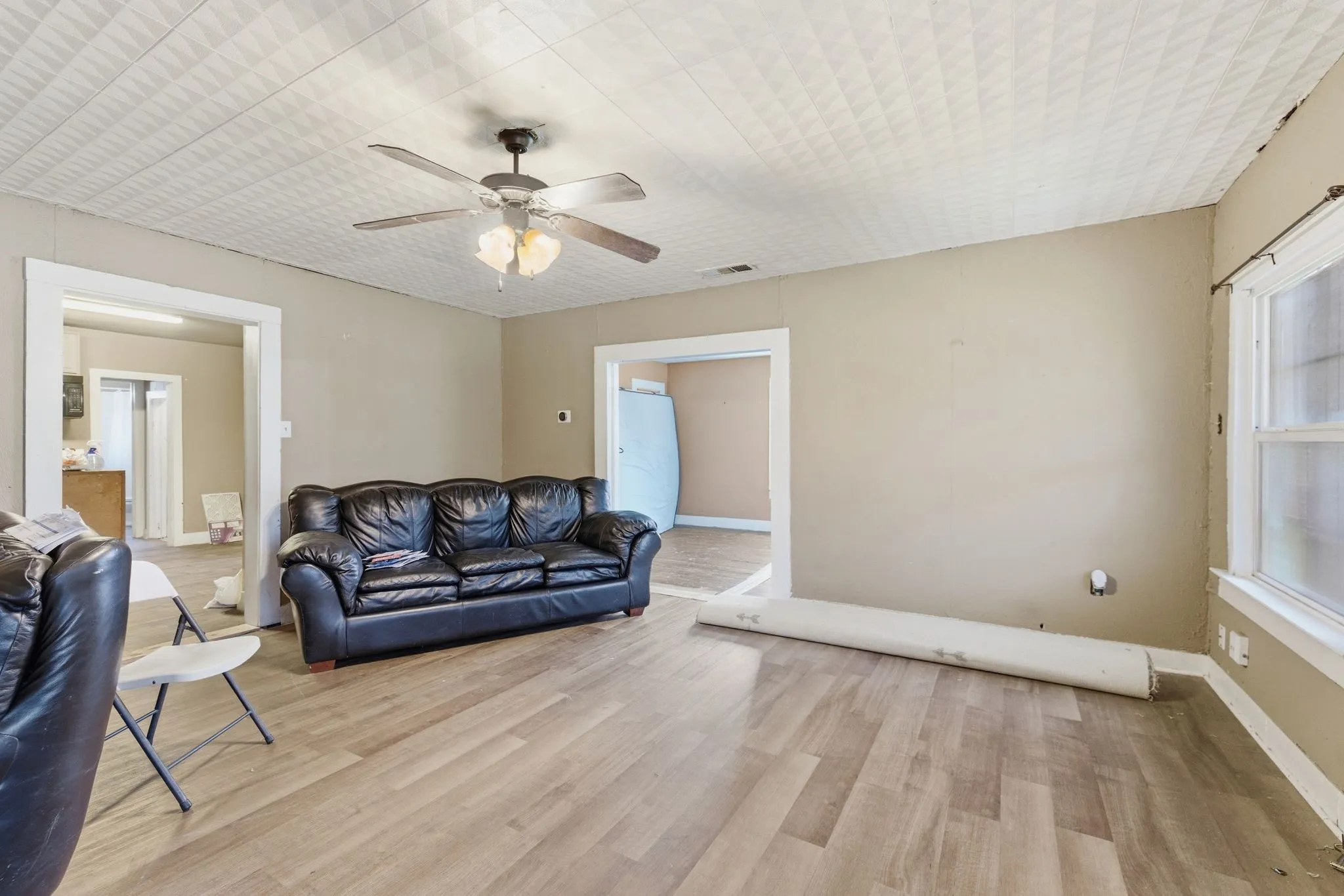 Spacious room featuring wood-finish flooring, light tan walls, and a patterned ceiling with a mounted ceiling fan