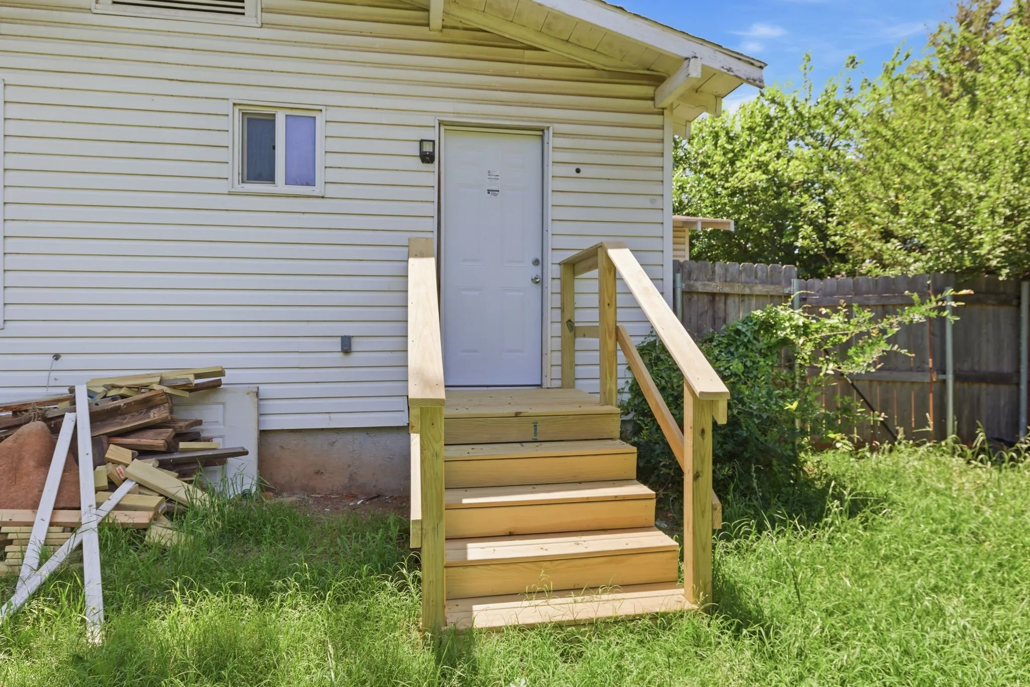 Exterior entry featuring a newly constructed wooden staircase with handrails, white siding, and a white entry door