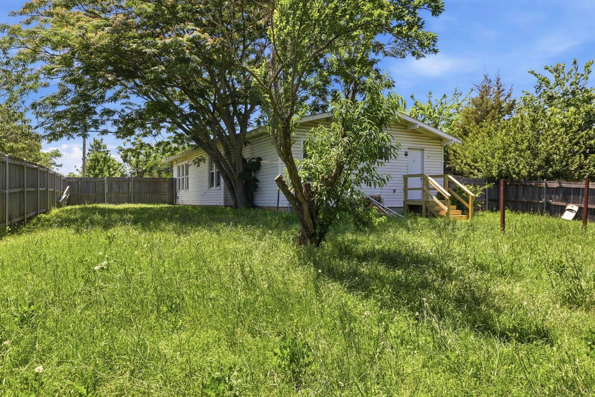 White siding residence with a wooden entry deck and steps, surrounded by a fenced perimeter