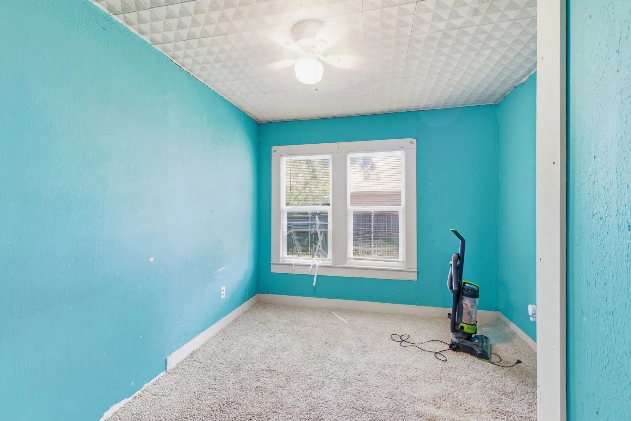 Room featuring textured walls, a ceiling fan with integrated lighting, a window with white trim, and light-colored carpet flooring