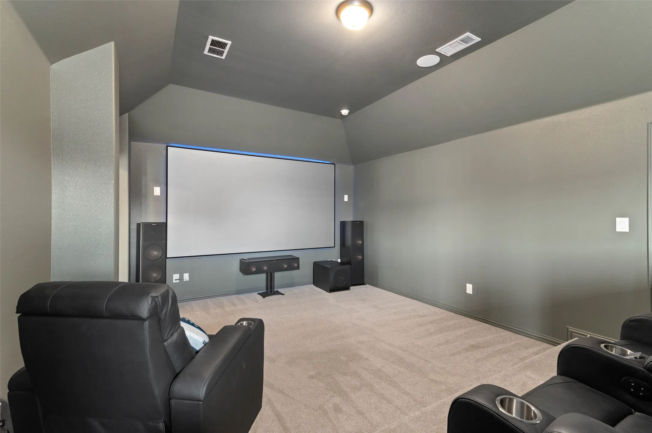 Dedicated media room featuring a large projection screen, dark painted walls, vaulted ceilings, recessed ceiling lighting, and carpet flooring