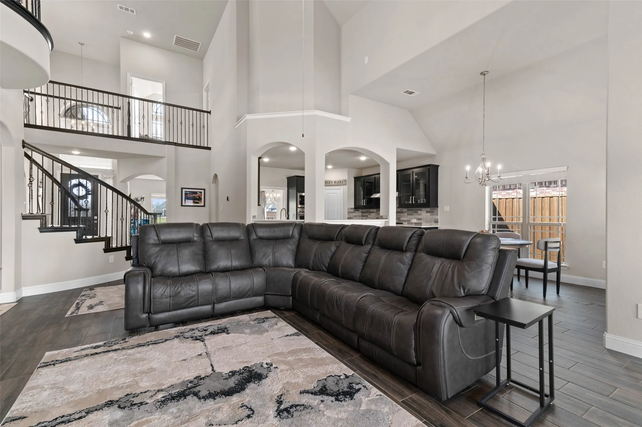 Two-story living area featuring wood-finish flooring, a grand staircase with wrought iron balusters, arched doorways, a high ceiling, and a dining space with a chandelier