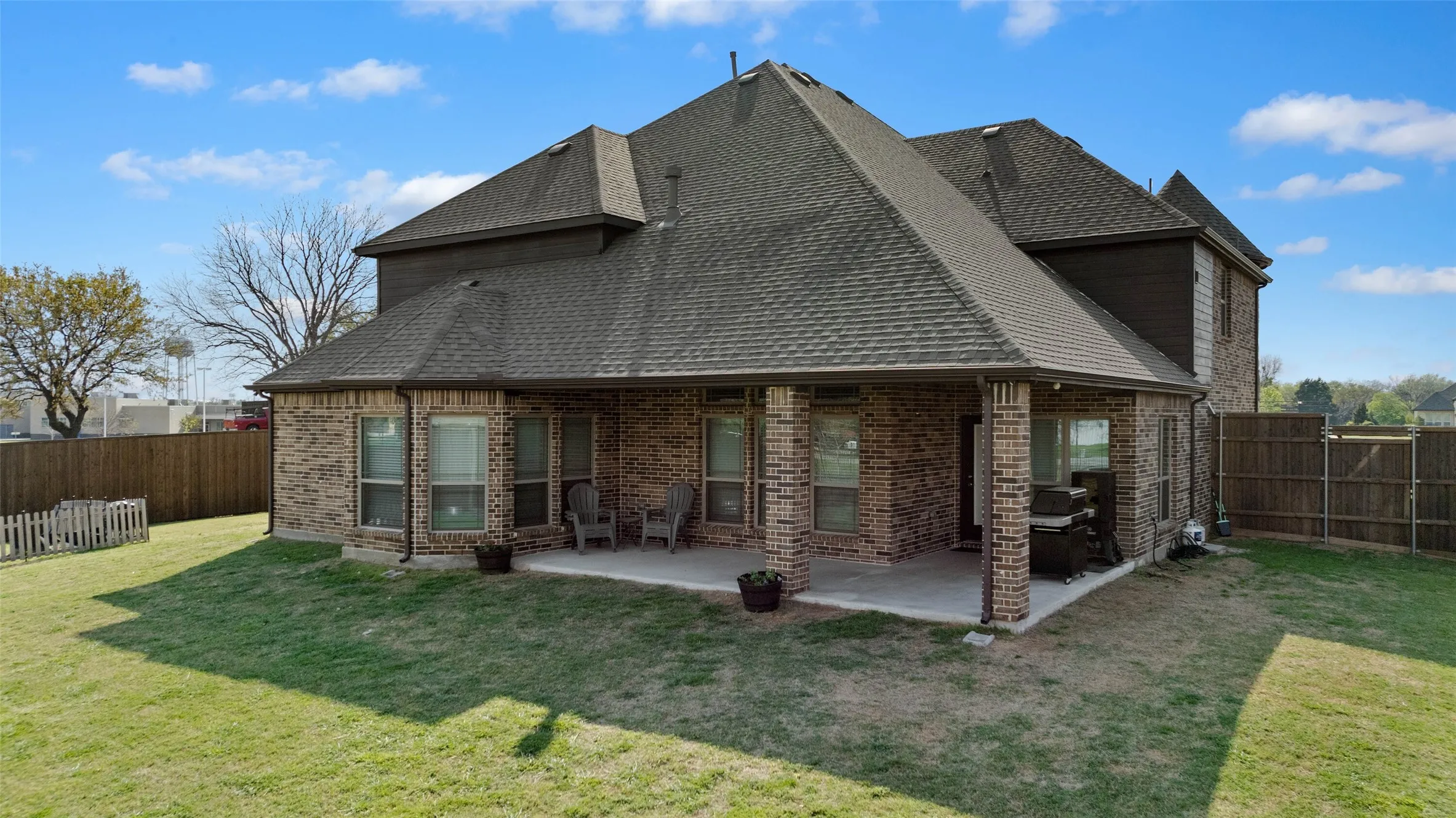 Expansive backyard featuring a covered patio with brick columns, a full privacy fence, and a manicured lawn