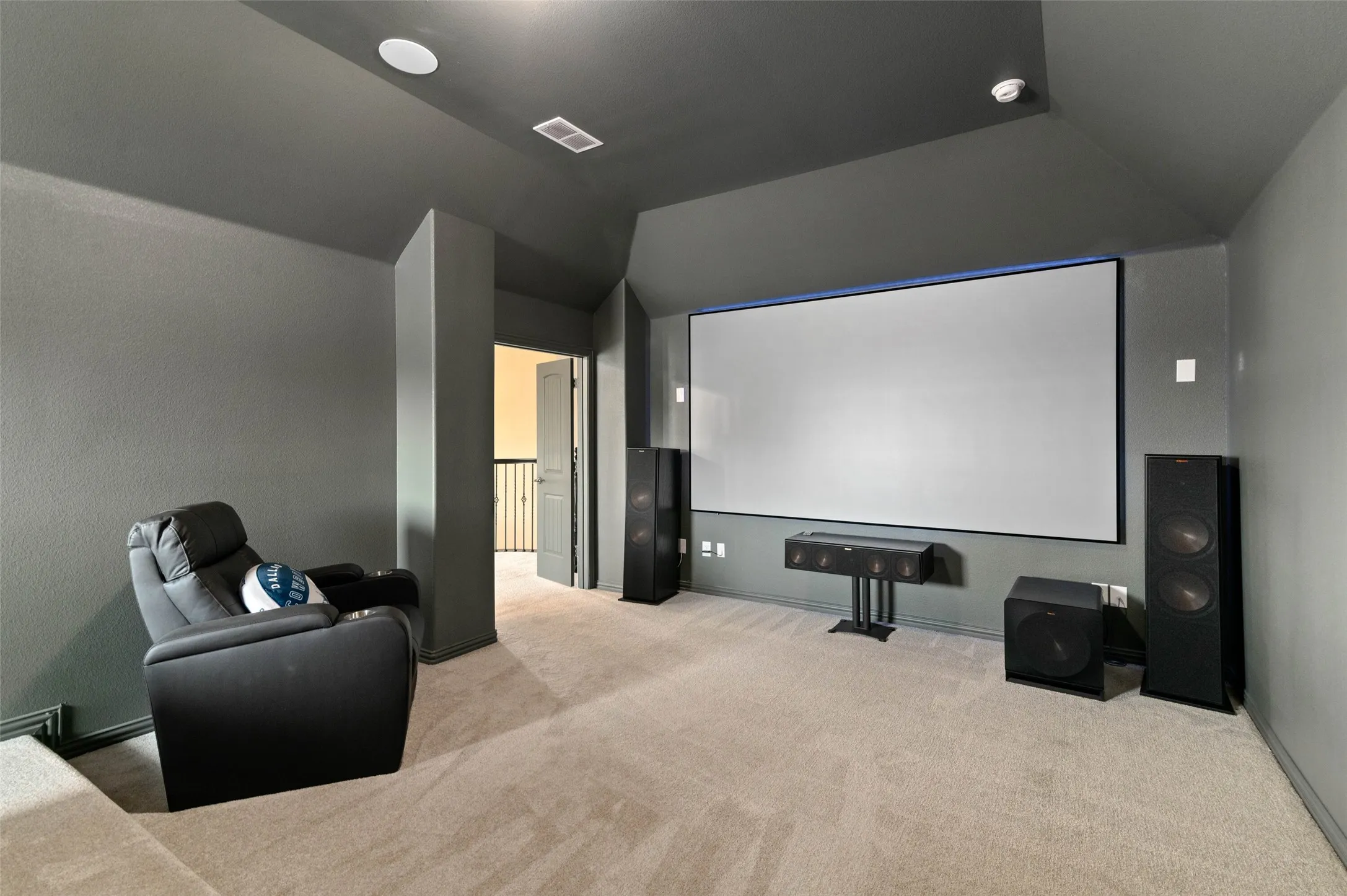 Dedicated media room featuring a large projection screen, recessed lighting, and neutral-toned carpeting