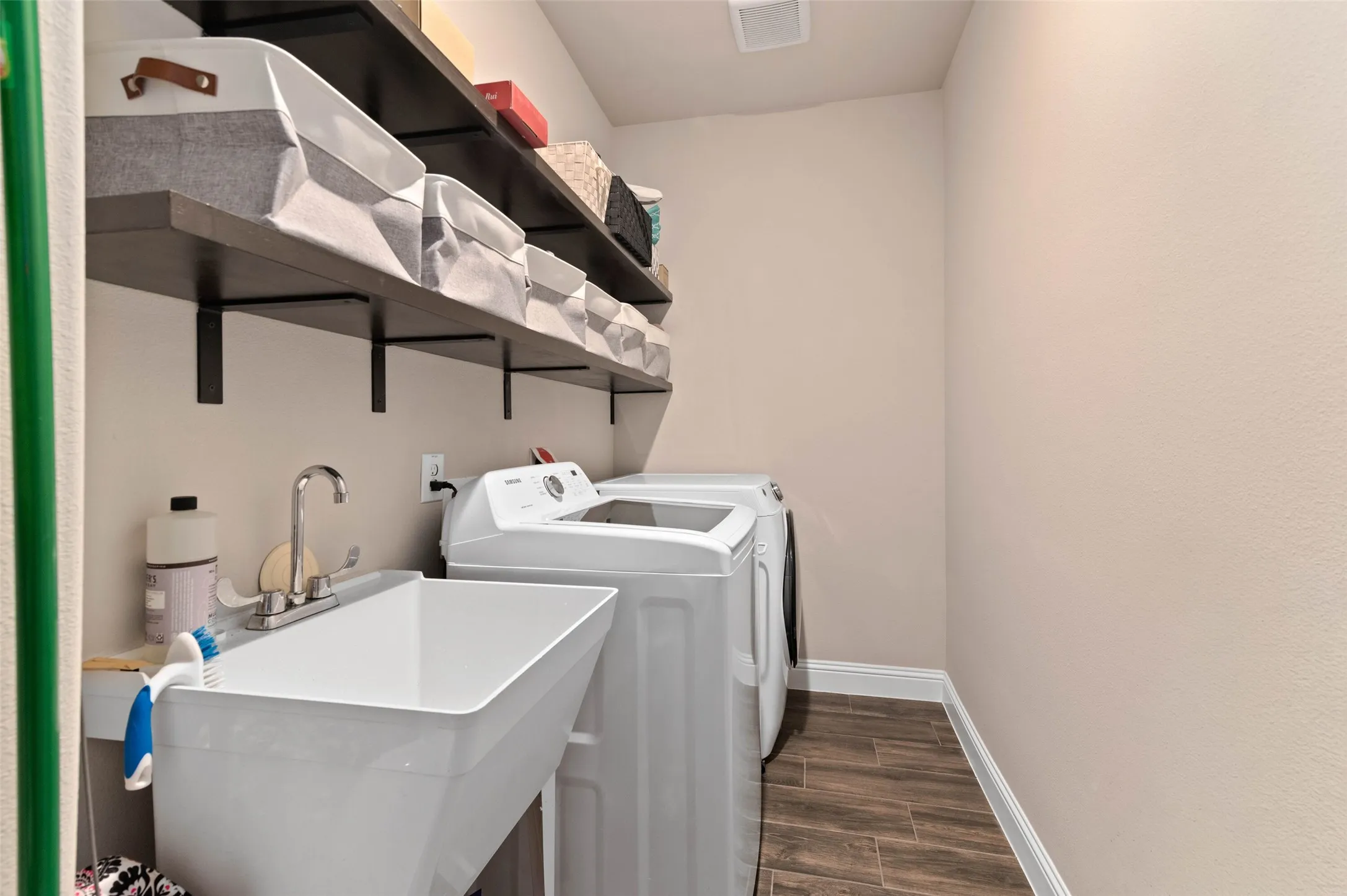 Dedicated laundry area featuring wood-finish tile flooring, a utility sink with a chrome faucet, and integrated shelving