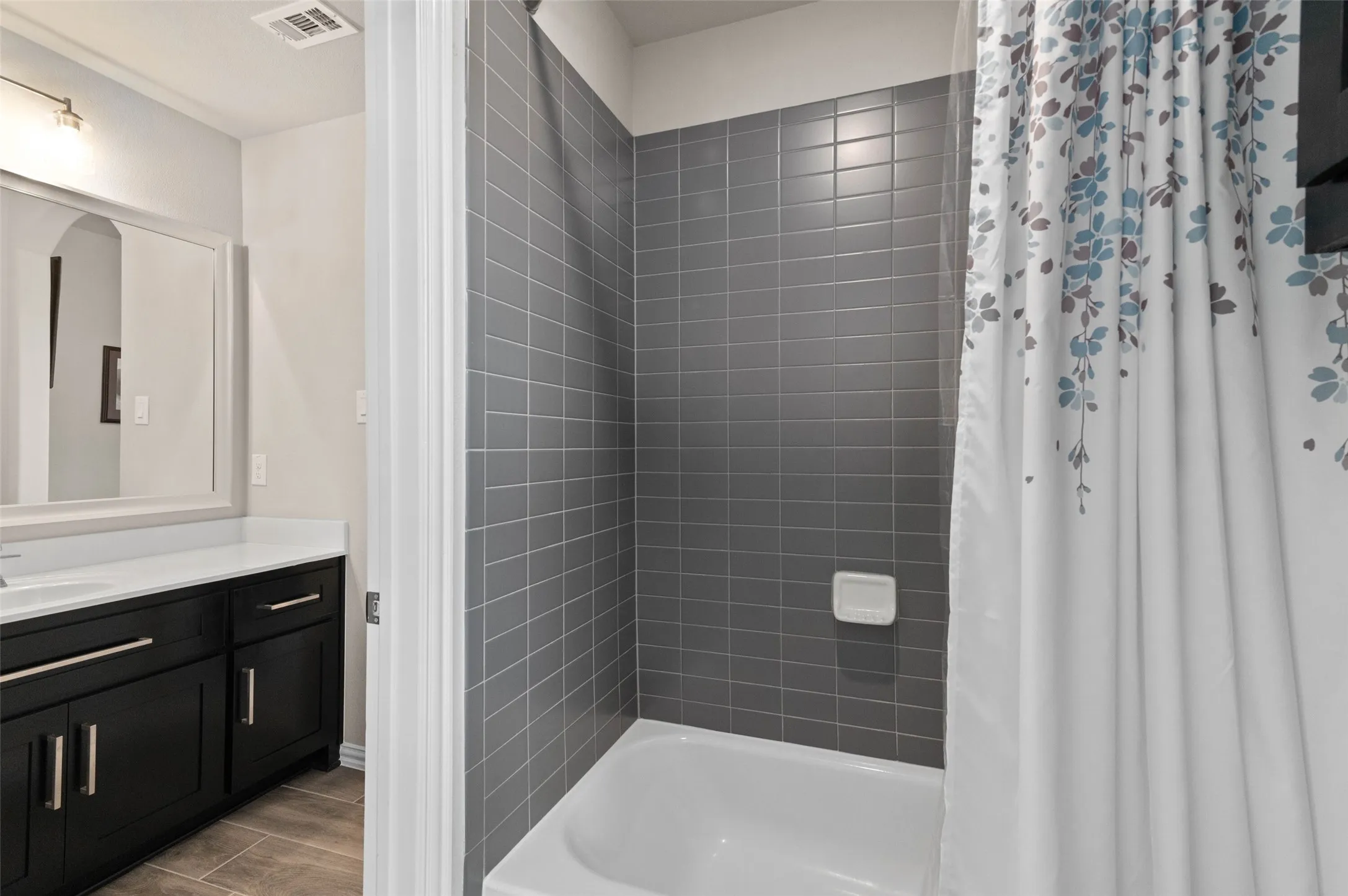 Bathroom featuring a white tub, gray subway tile surround, dark wood-finish vanity with a white countertop, and a framed mirror