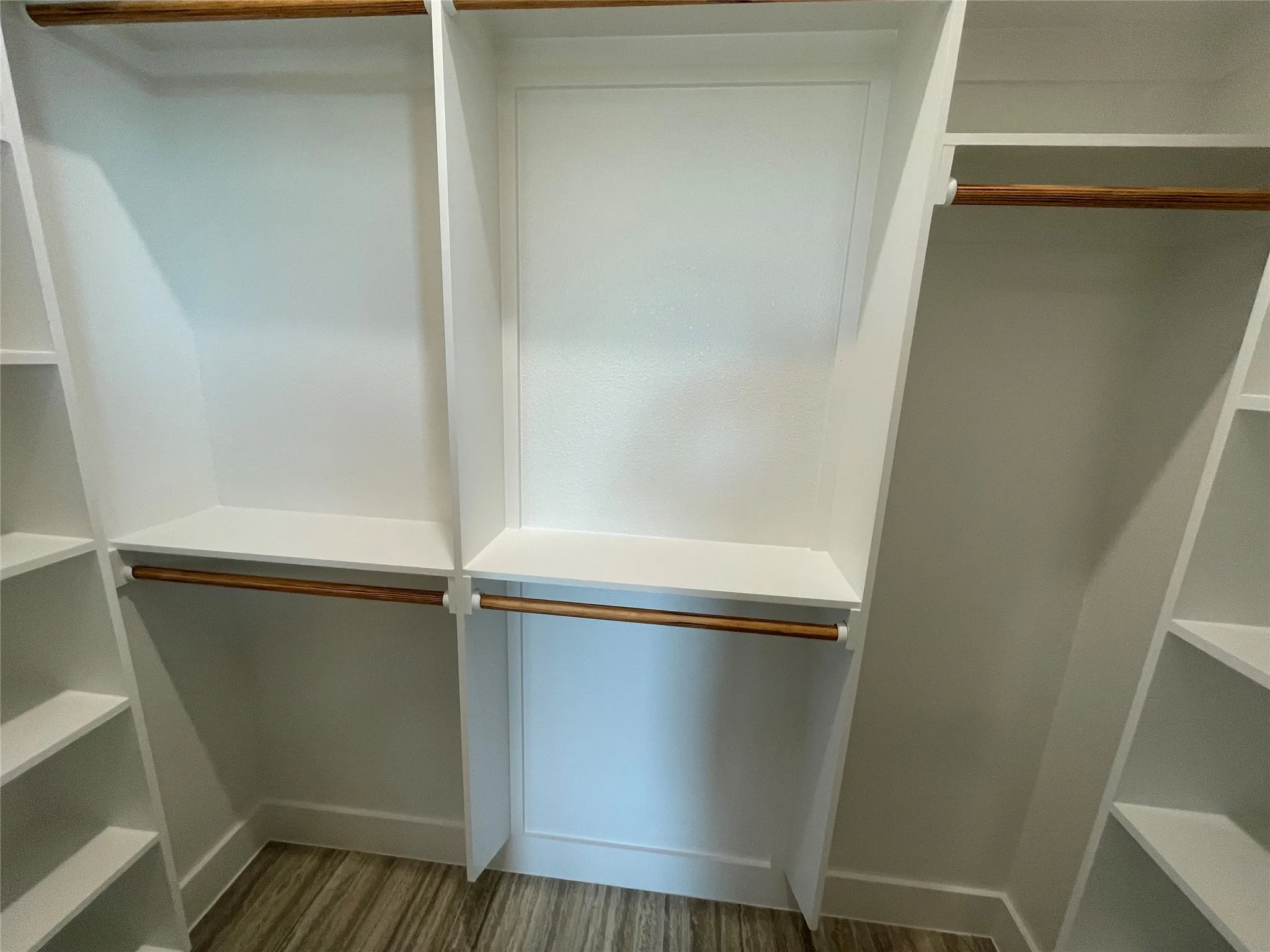 Custom closet system featuring white built-in shelving, wood-finish hanging rods, and wood-finish flooring