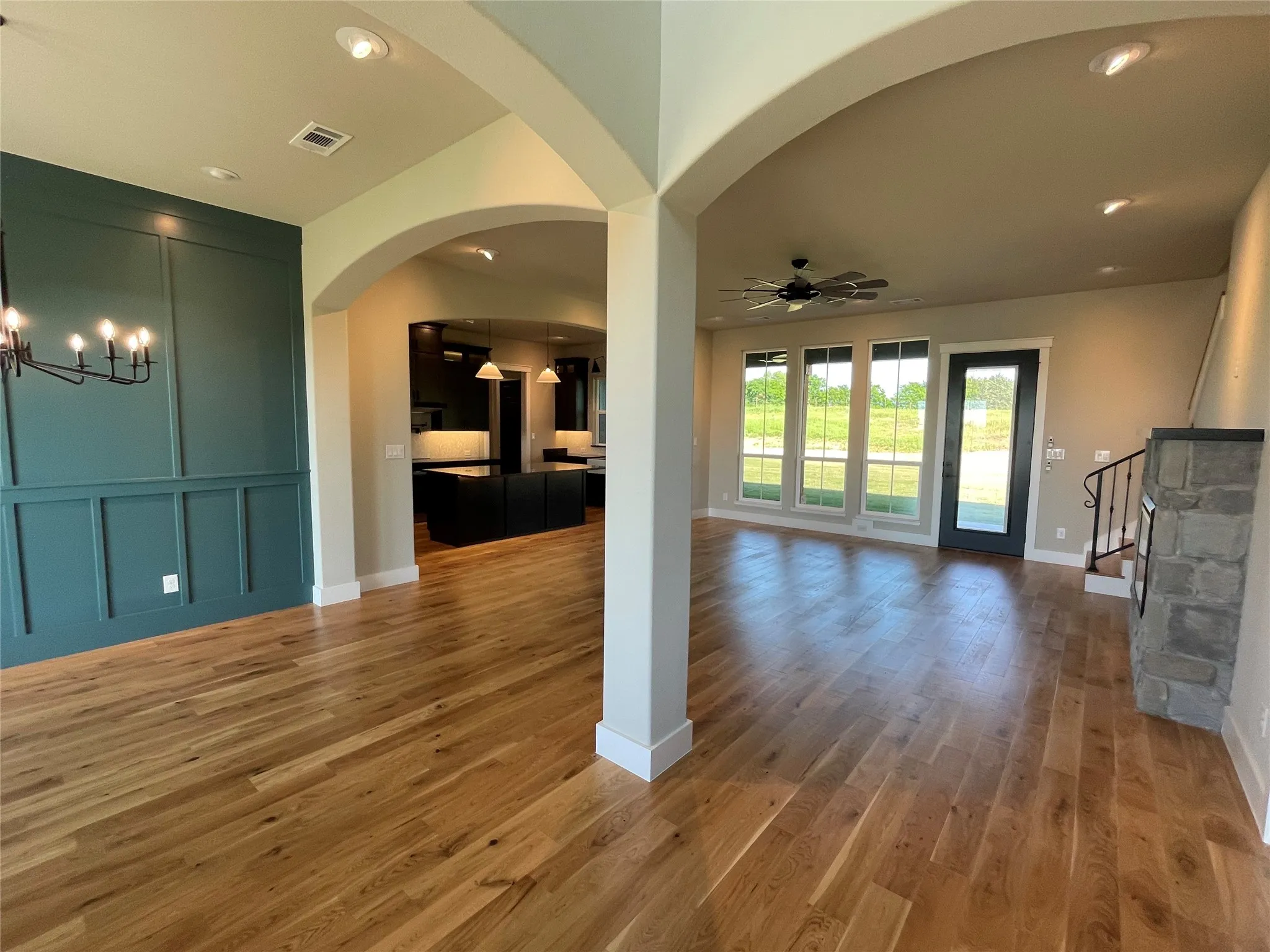 Expansive open-concept interior featuring light wood-finish flooring, arched doorways, a board and batten accent wall, recessed lighting, and large windows