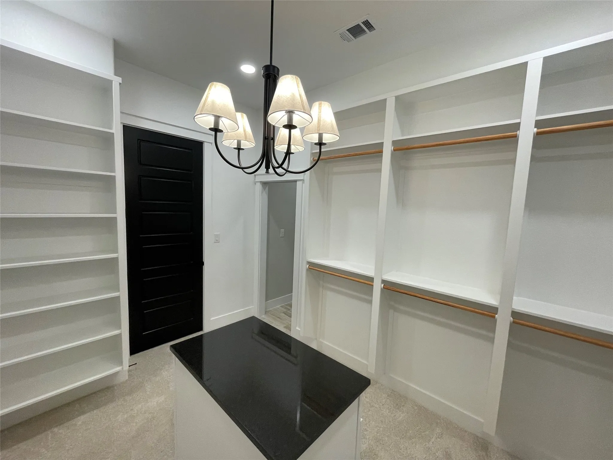 Custom closet system featuring extensive shelving, hanging rods, a central island with a dark countertop, and a five-light chandelier