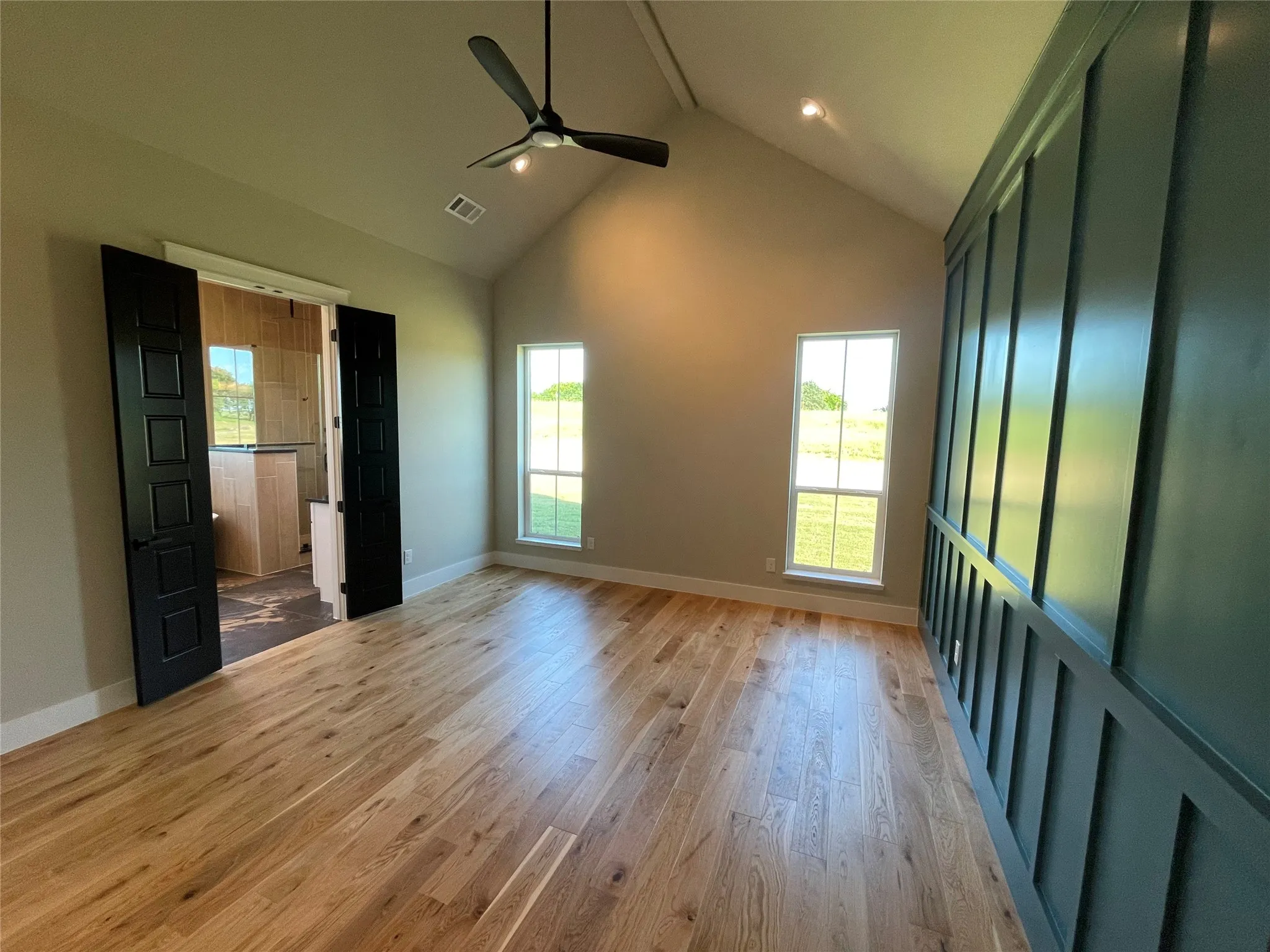 Spacious room featuring vaulted ceilings, light wood-finish flooring, and a modern ceiling fan