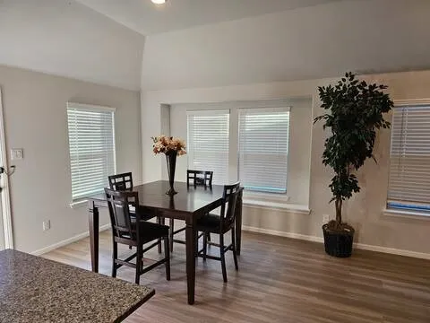 Dining area featuring vaulted ceilings, wood-finish flooring, a window seat, and multiple windows with blinds