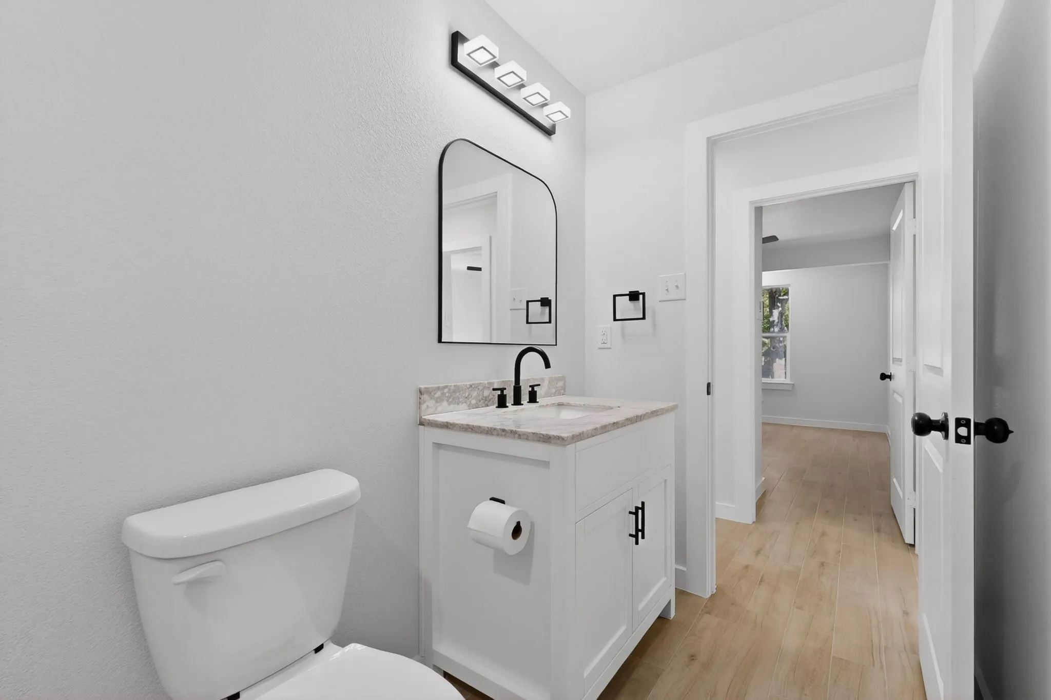 Bathroom featuring a white vanity with a stone-finish countertop, black hardware, an arched mirror, and a modern light fixture