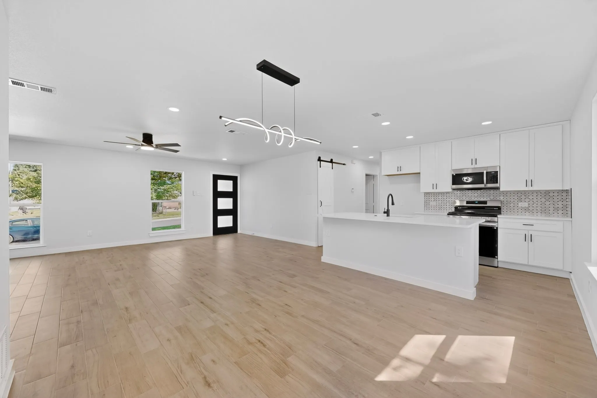 Spacious open-concept living area featuring wood-finish flooring and a contemporary linear light fixture