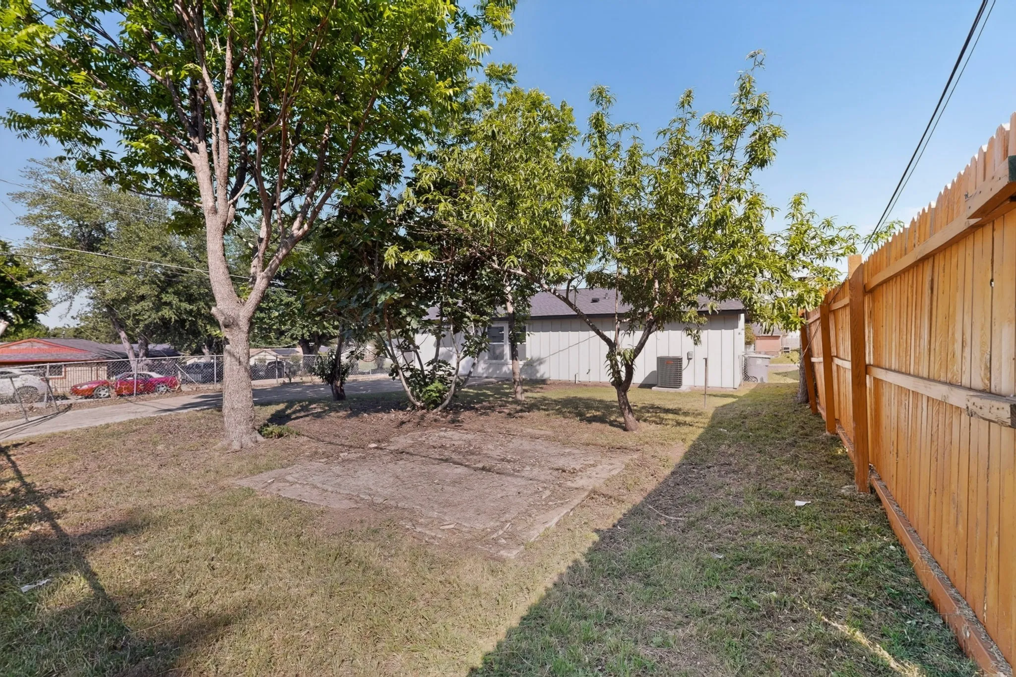 Expansive grassy yard with mature trees, a privacy fence, and a concrete pad