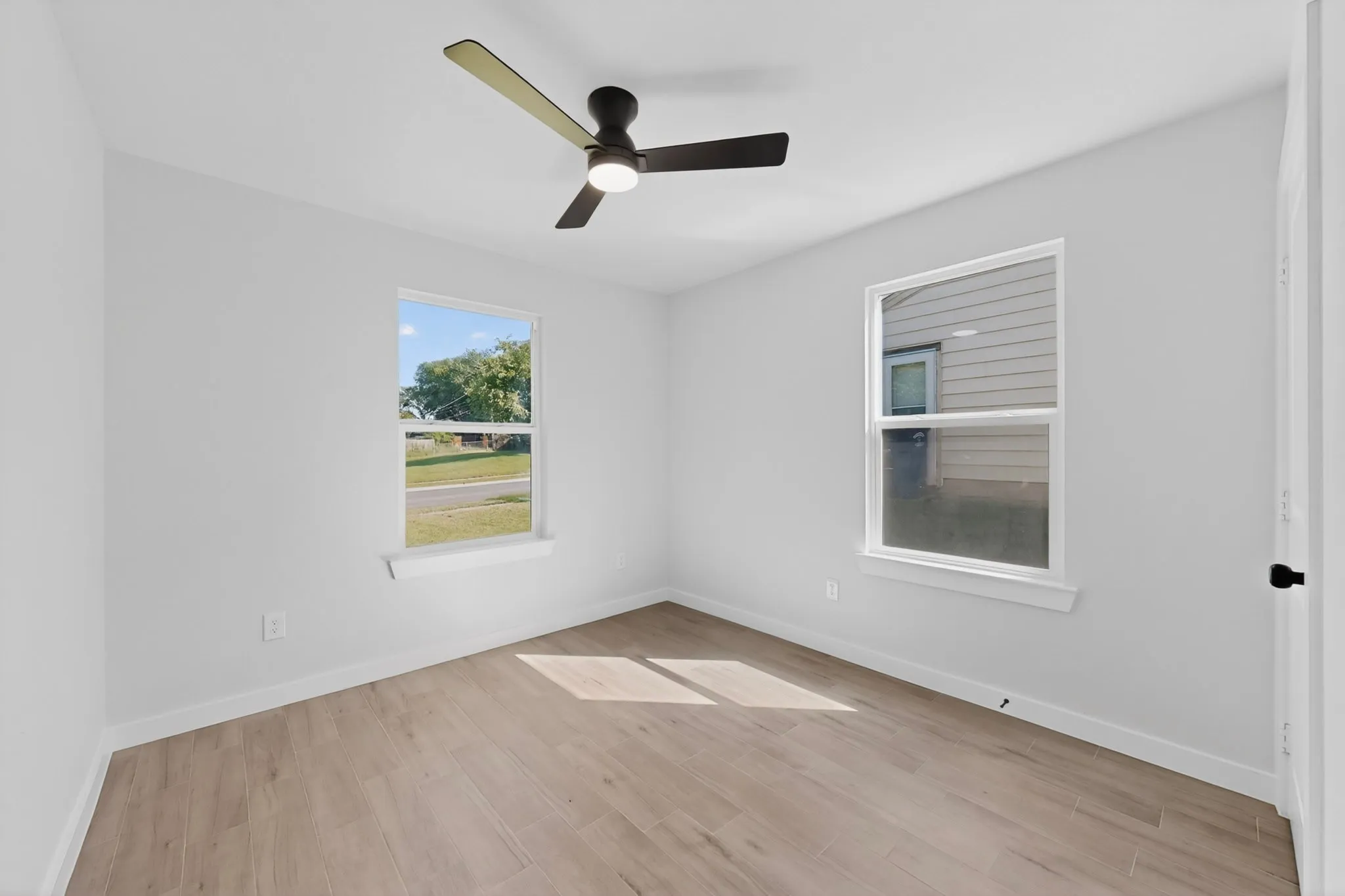 Bright room featuring two windows, light wood-finish flooring, white baseboards, and a contemporary ceiling fan with​​‌​​​​‌​​‌‌​‌‌​​​‌‌​‌​‌​‌​​​‌​​ lighting