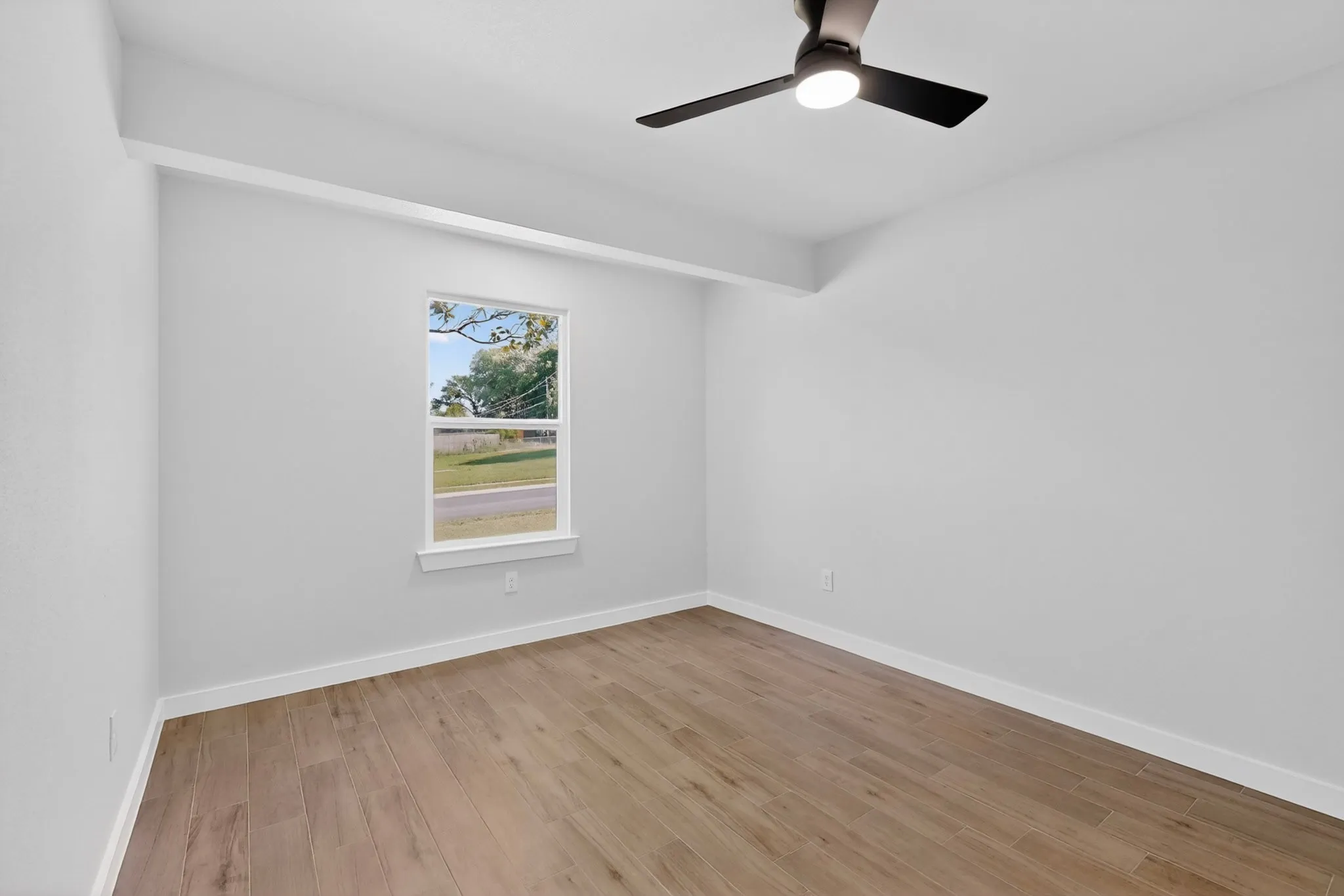 Bright interior space featuring wood-finish flooring, a contemporary ceiling fan with integrated lighting, and a window with white trim