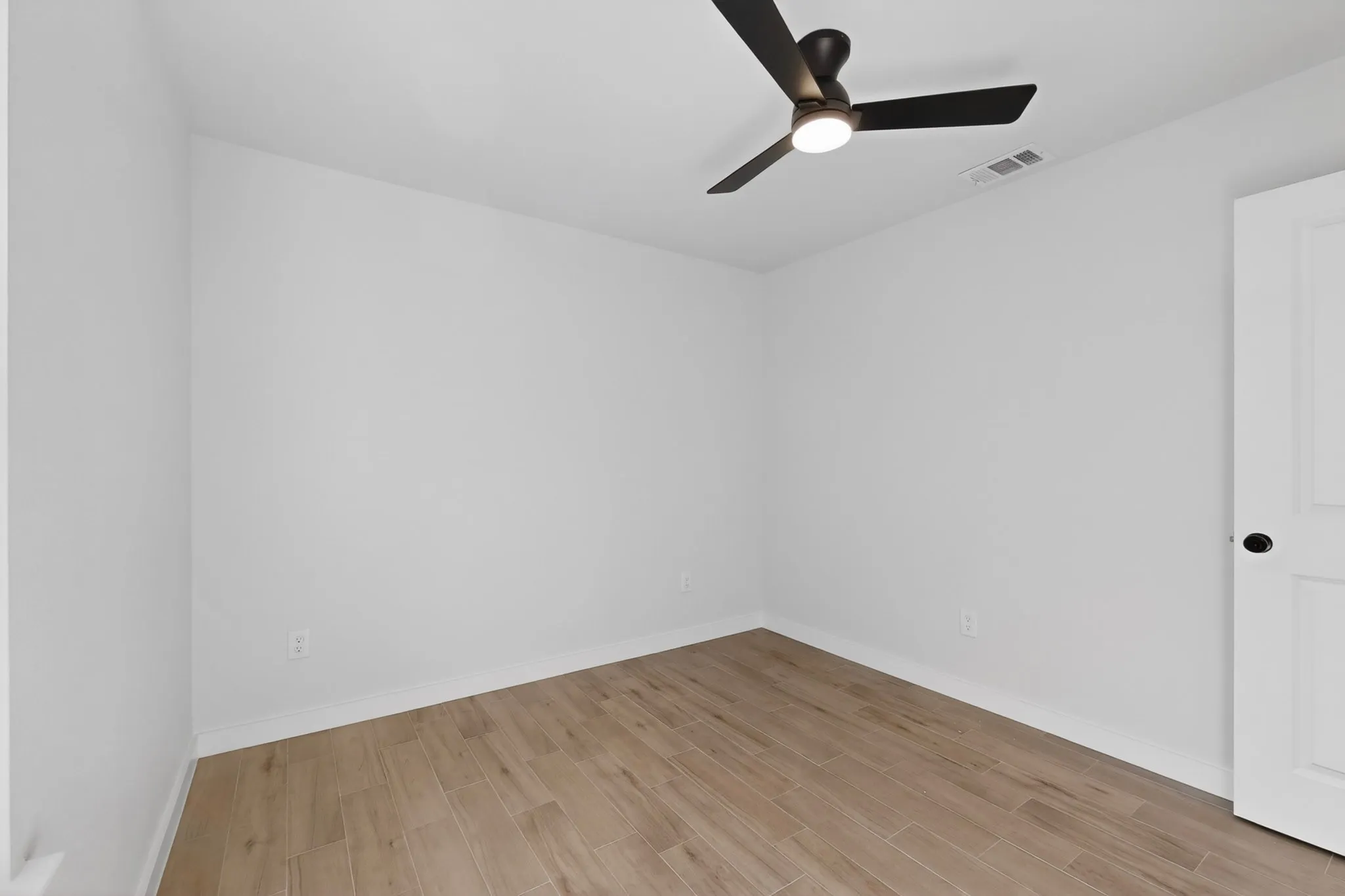 Neutral white walls, wood-finish flooring, and a contemporary ceiling fan with integrated lighting