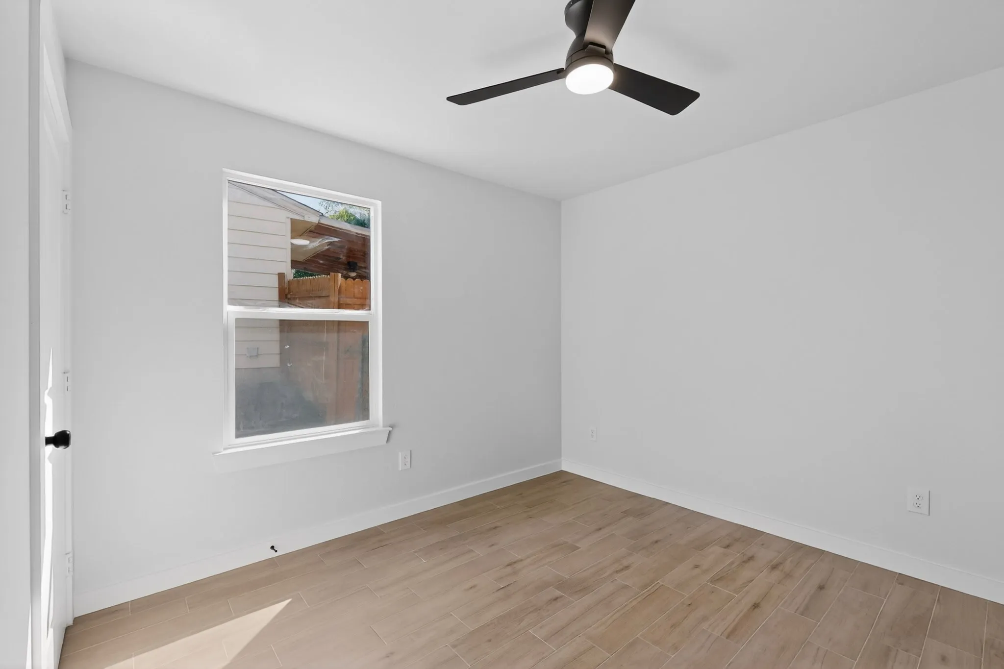 Room featuring light-toned wood-finish flooring, a contemporary ceiling fan with integrated lighting, a single window, and a white interior door with matte black hardware